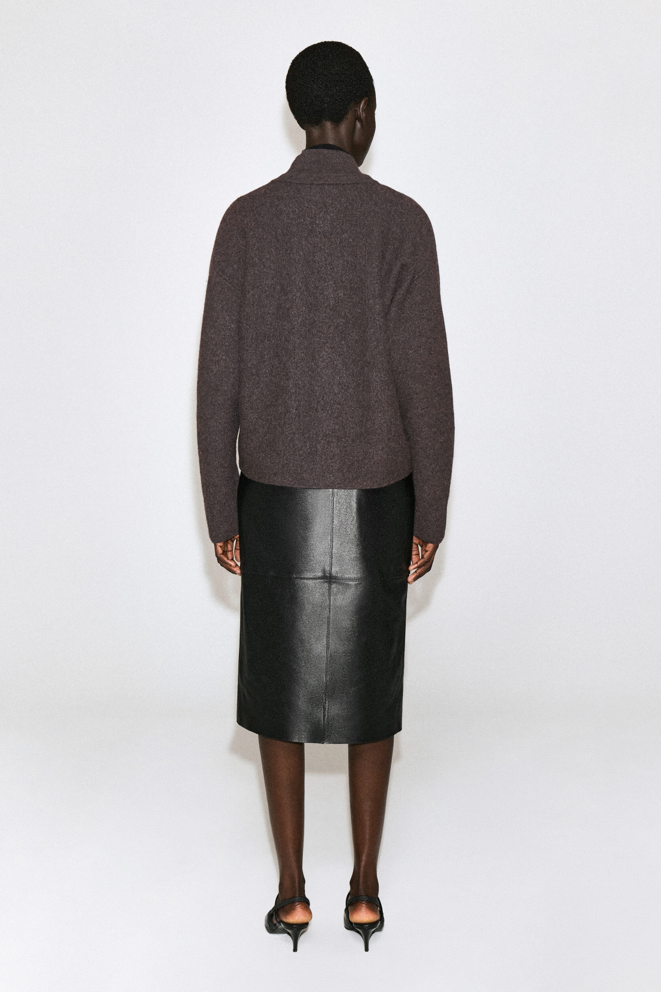 Un cardigan en laine bouillie brun est présenté de dos, mettant en valeur sa silhouette légèrement arrondie, ses épaules tombantes et son col montant. Le cardigan à coupe régulière arrive aux hanches et est agencé avec une jupe en cuir noir. Un cardigan en laine bouillie brun est présenté de dos, mettant en valeur sa silhouette légèrement arrondie, ses épaules tombantes et son col montant. Le cardigan à coupe régulière arrive aux hanches et est agencé avec une jupe en cuir noir.