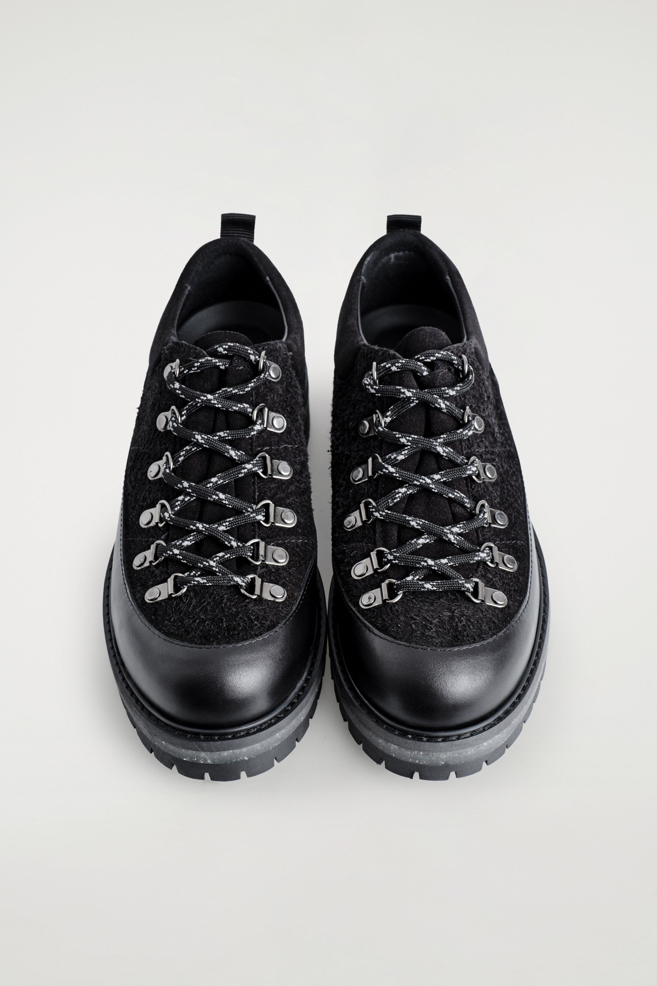 Ver imagen más grande: Dos zapatos negros de corte bajo se presentan desde una vista frontal superior, con partes superiores de gamuza texturizada y punteras de cuero liso. Están detallados con cordones de cuerda moteados en blanco y negro, enhebrados a través de ojales en forma de D de tono plateado y descansan sobre suelas gruesas en capas con una capa intermedia moteada de gris.