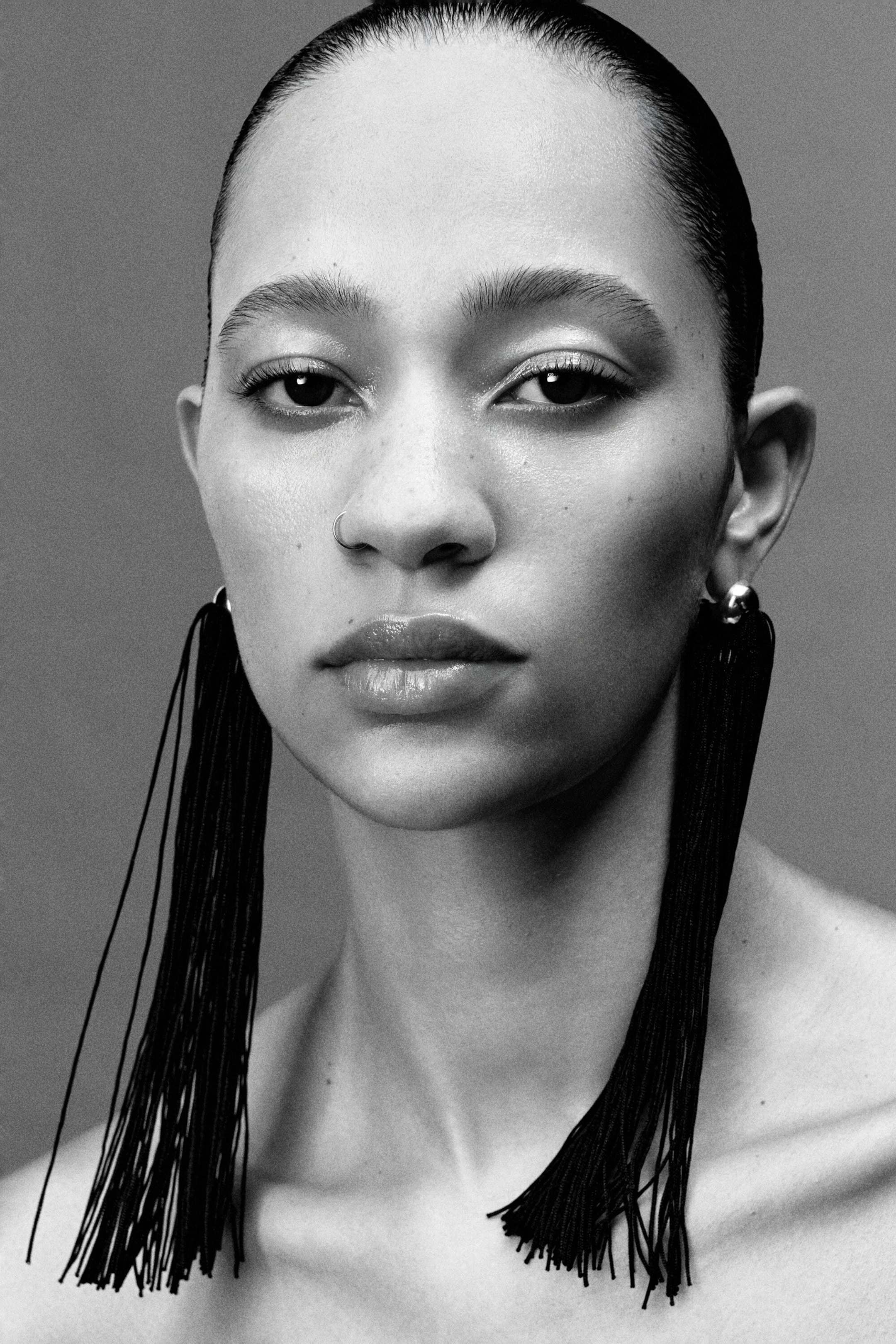Fringed earrings featuring small metallic spherical studs are hanging from the earlobes, with long, fine black thread strands cascading past the shoulders.