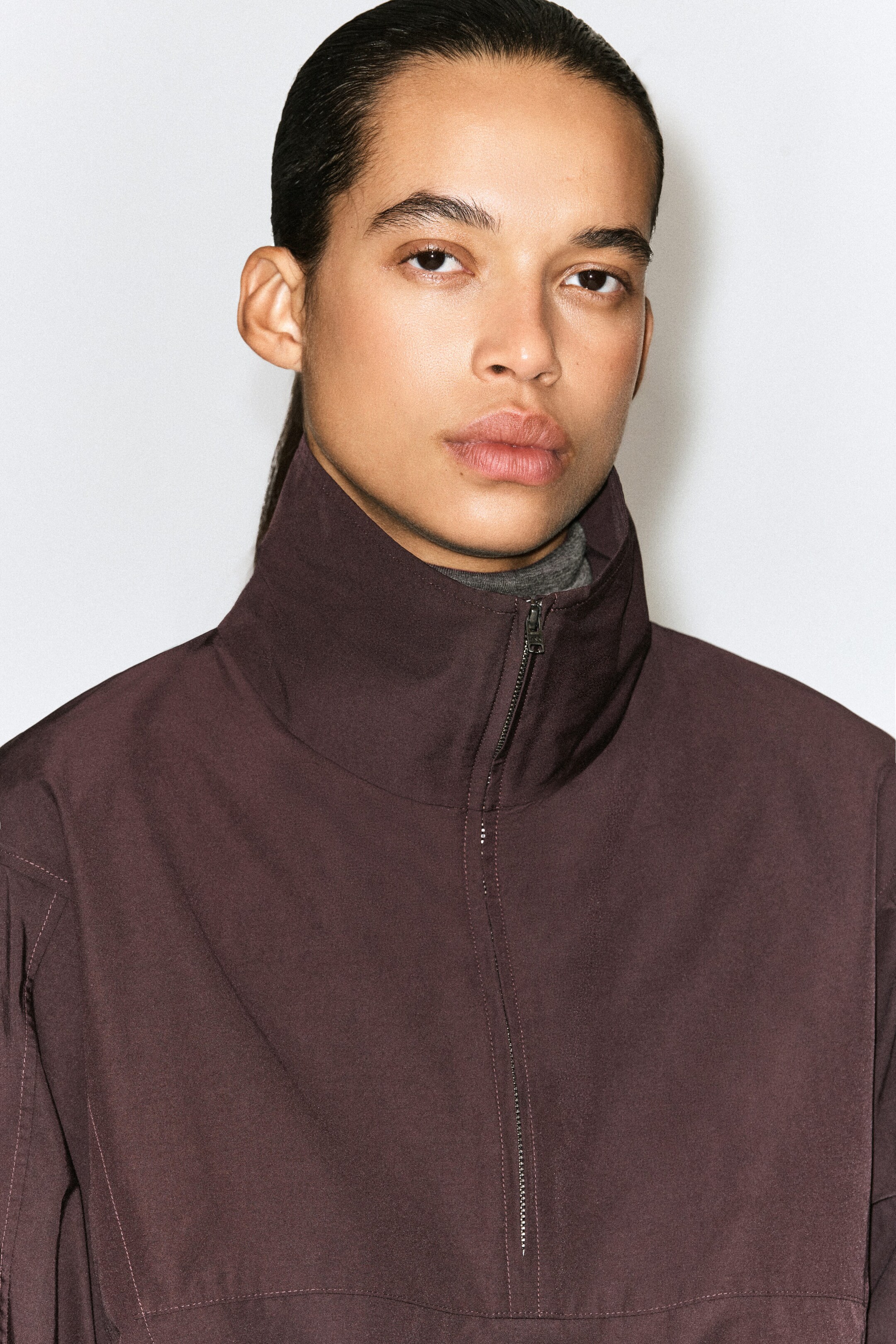 A dark brown zip-up shirt featuring a high stand-up collar, topstitched seams, and a silver-tone zipper is being worn over a grey turtleneck in a close-up front view. A dark brown zip-up shirt featuring a high stand-up collar, topstitched seams, and a silver-tone zipper is being worn over a grey turtleneck in a close-up front view.