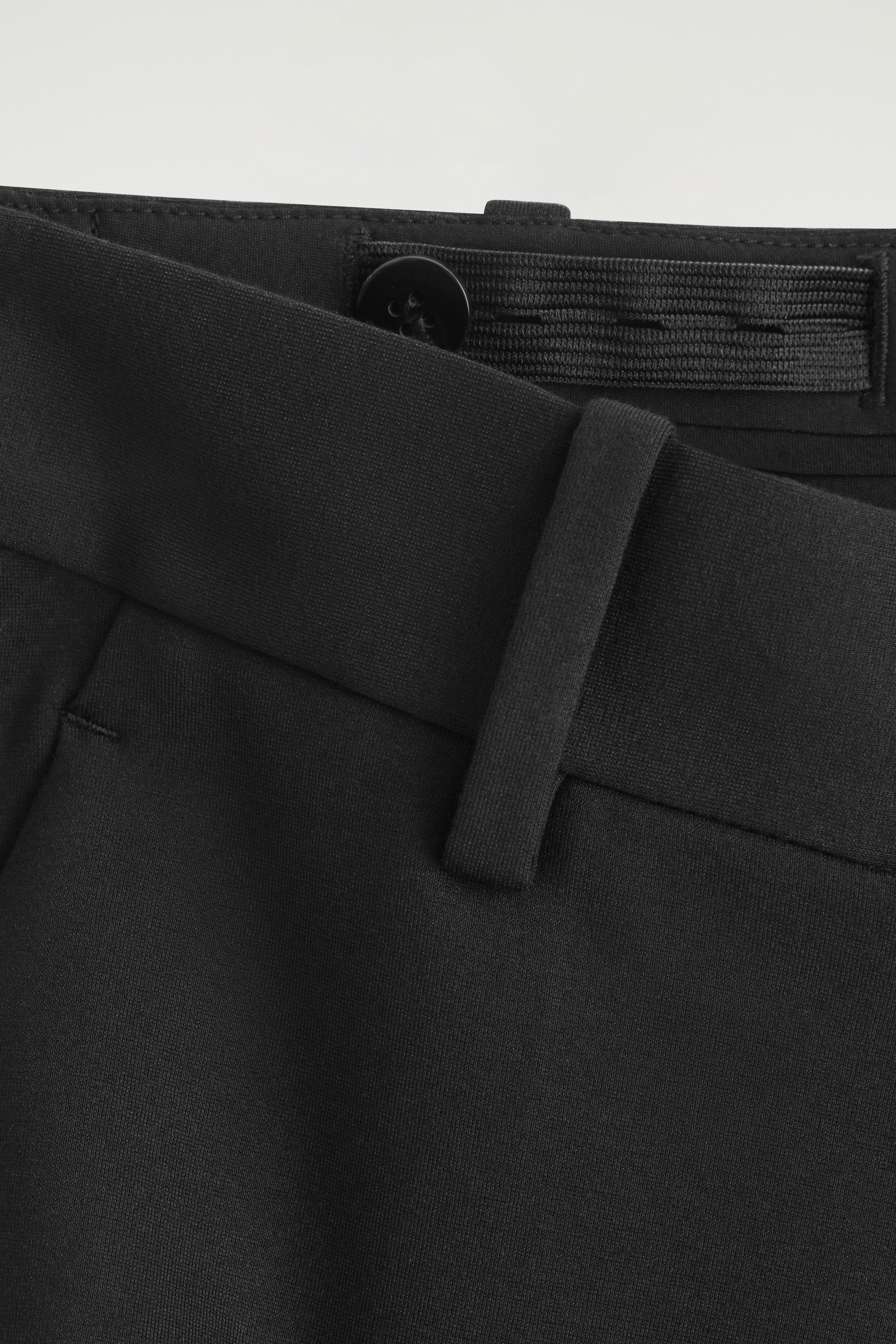 Agrandir l'image: Un pantalon noir montre un gros plan de la ceinture, avec une bande élastique intérieure réglable et un bouton noir. Un seul passant de ceinture est également visible à l'avant de la ceinture.