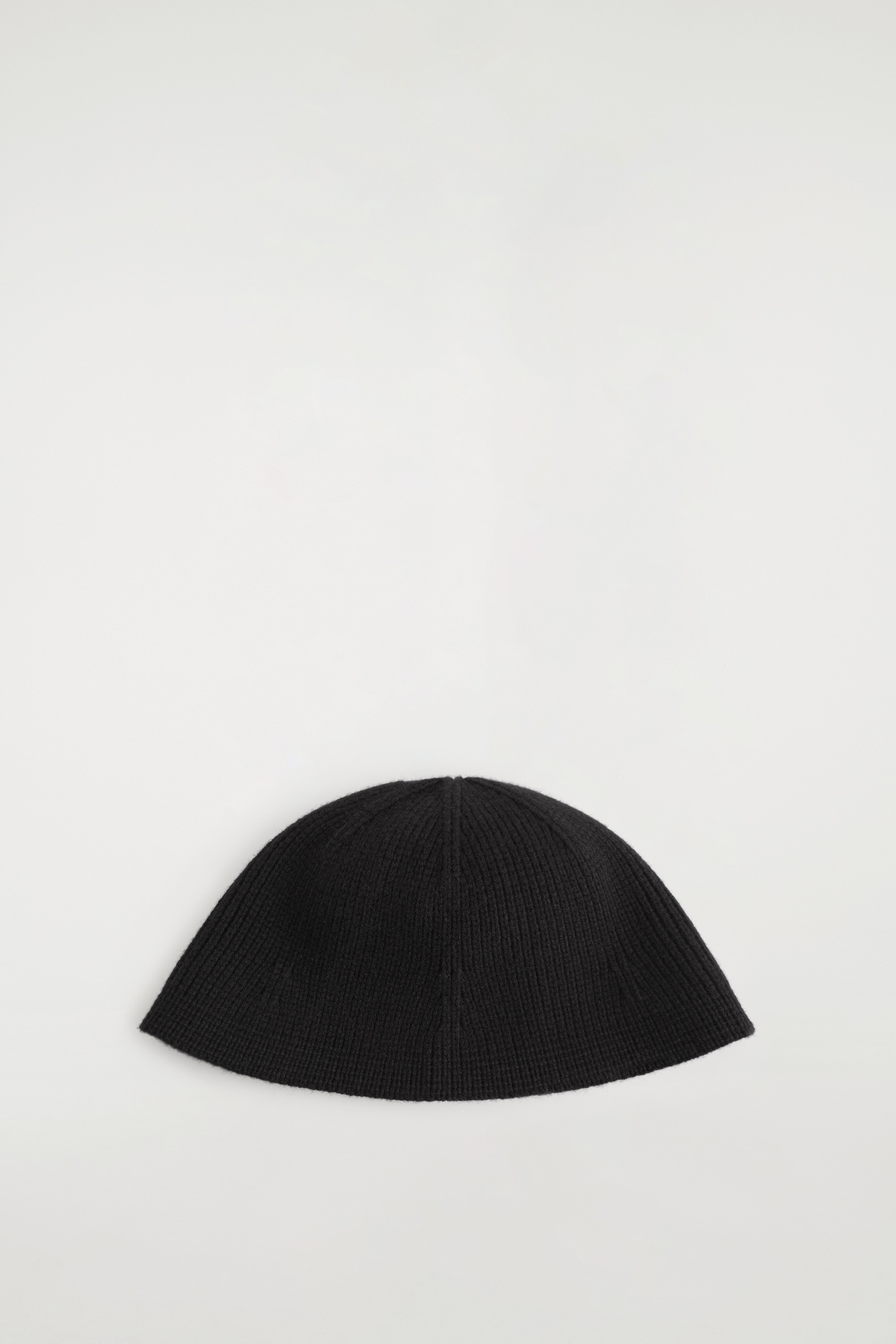 Ein schwarzer Bucket Hat aus Rippstrick mit strukturierter, runder Silhouette wird vom Model getragen. Der Hut ist mit einer schwarzen Lederjacke mit breiten Revers kombiniert.