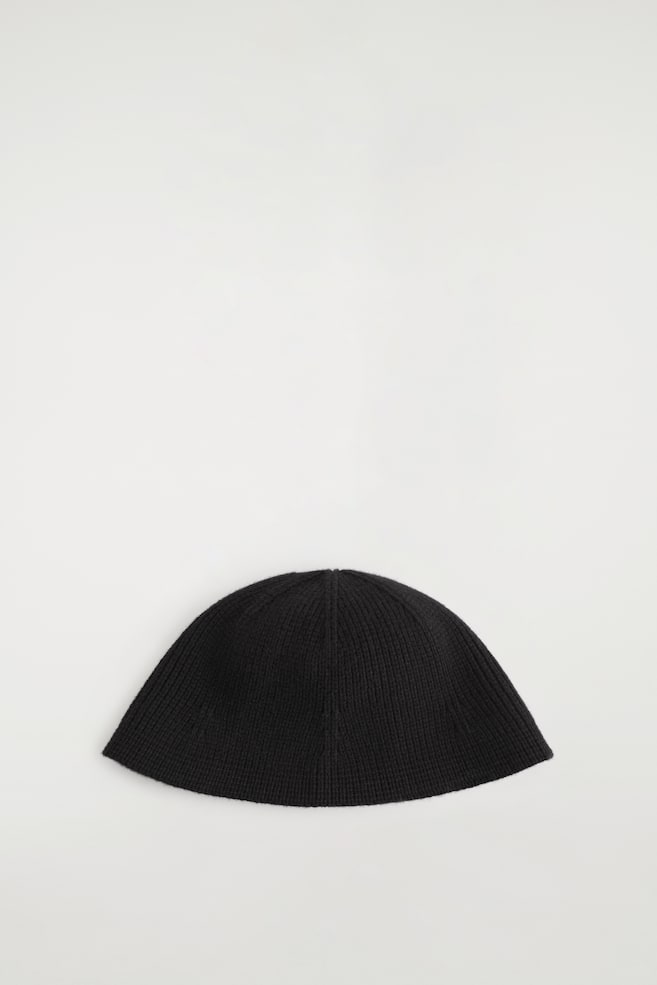 Un chapeau bob noir en maille est présenté de face, avec une silhouette en dôme structurée et une fine texture côtelée. Le chapeau met en valeur des coutures de panneaux nettes qui dessinent son design sculpté, légèrement évasé. - 1