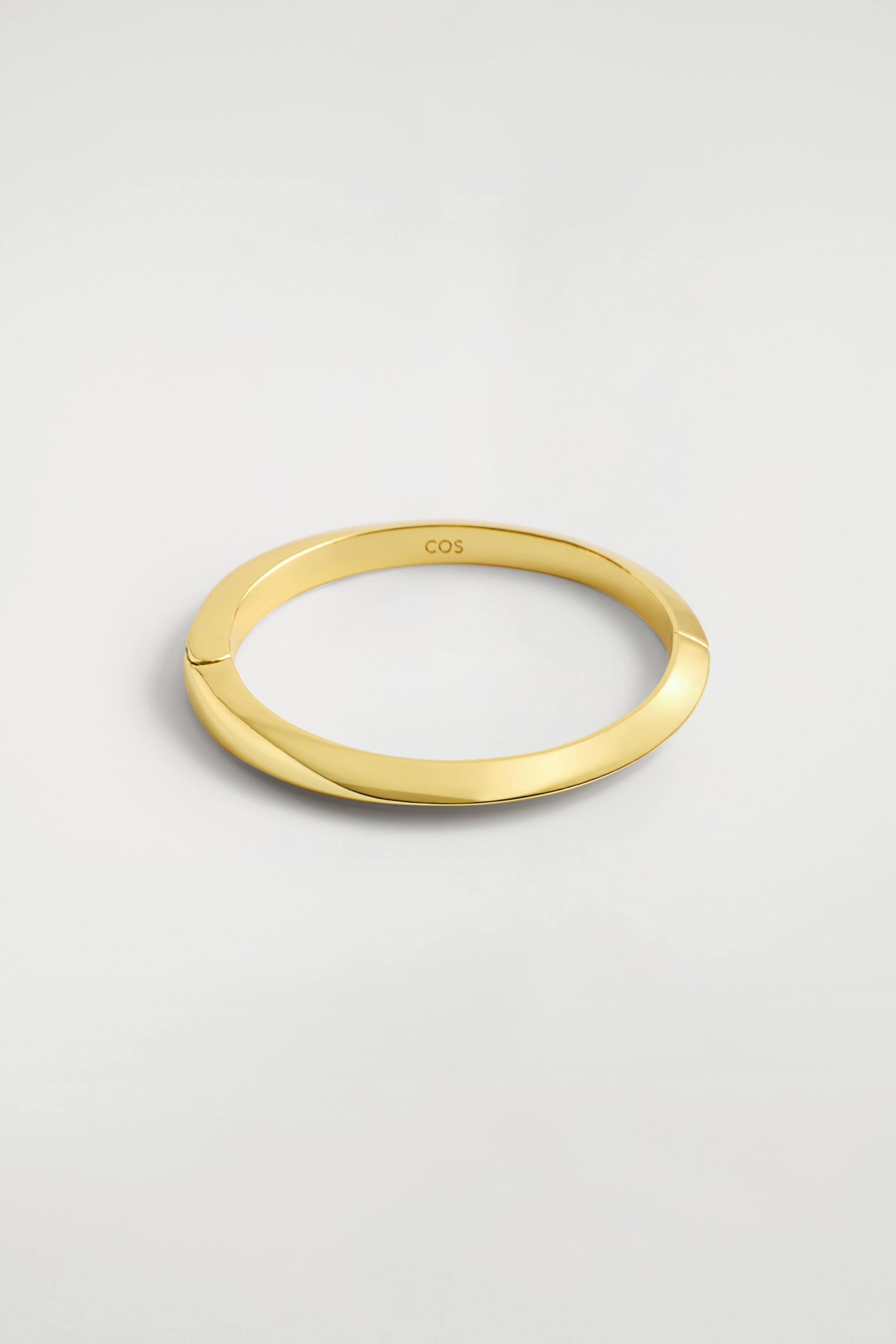 Visualizza immagine più grande: Il bracciale rigido sfaccettato presenta una finitura color oro e superfici angolari distintive lungo tutta la circonferenza. Su un lato è visibile un meccanismo a cerniera.