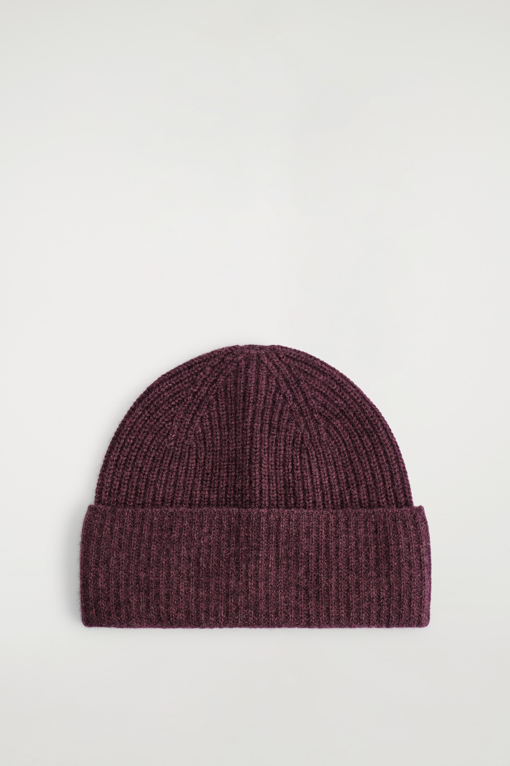 View larger image: A dark plum-colored beanie is being displayed, featuring a prominent ribbed knit pattern throughout its rounded top and body. A wide, folded ribbed cuff is forming the bottom edge of the beanie.