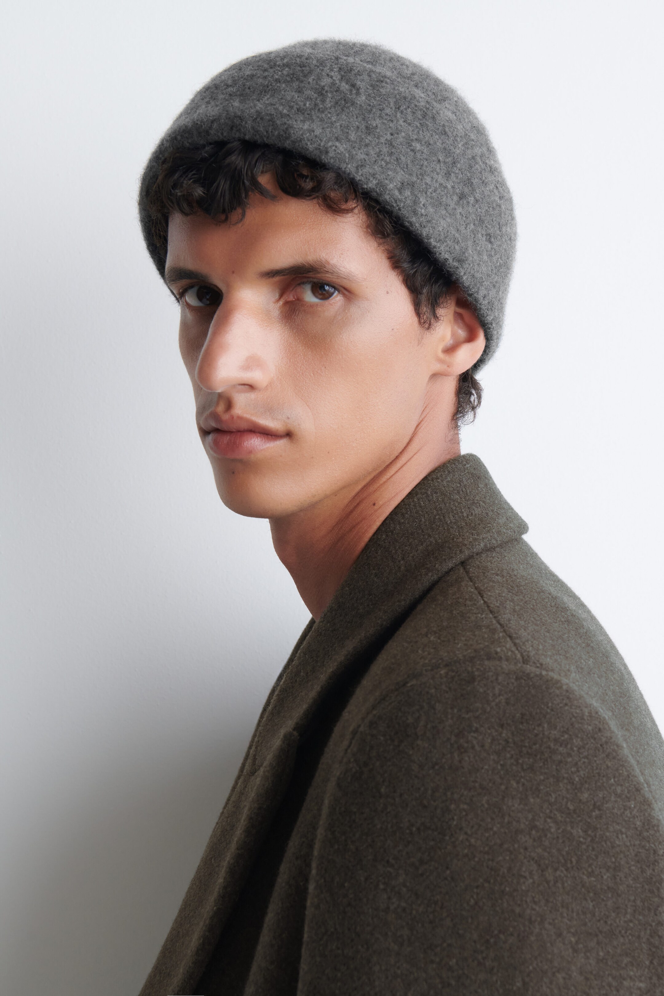 Un bonnet tricoté texturé gris est porté par le modèle, ajusté parfaitement sur la tête. Le bonnet est stylisé avec un manteau en laine vert foncé doté d’un col structuré. Un bonnet tricoté texturé gris est porté par le modèle, ajusté parfaitement sur la tête. Le bonnet est stylisé avec un manteau en laine vert foncé doté d’un col structuré.