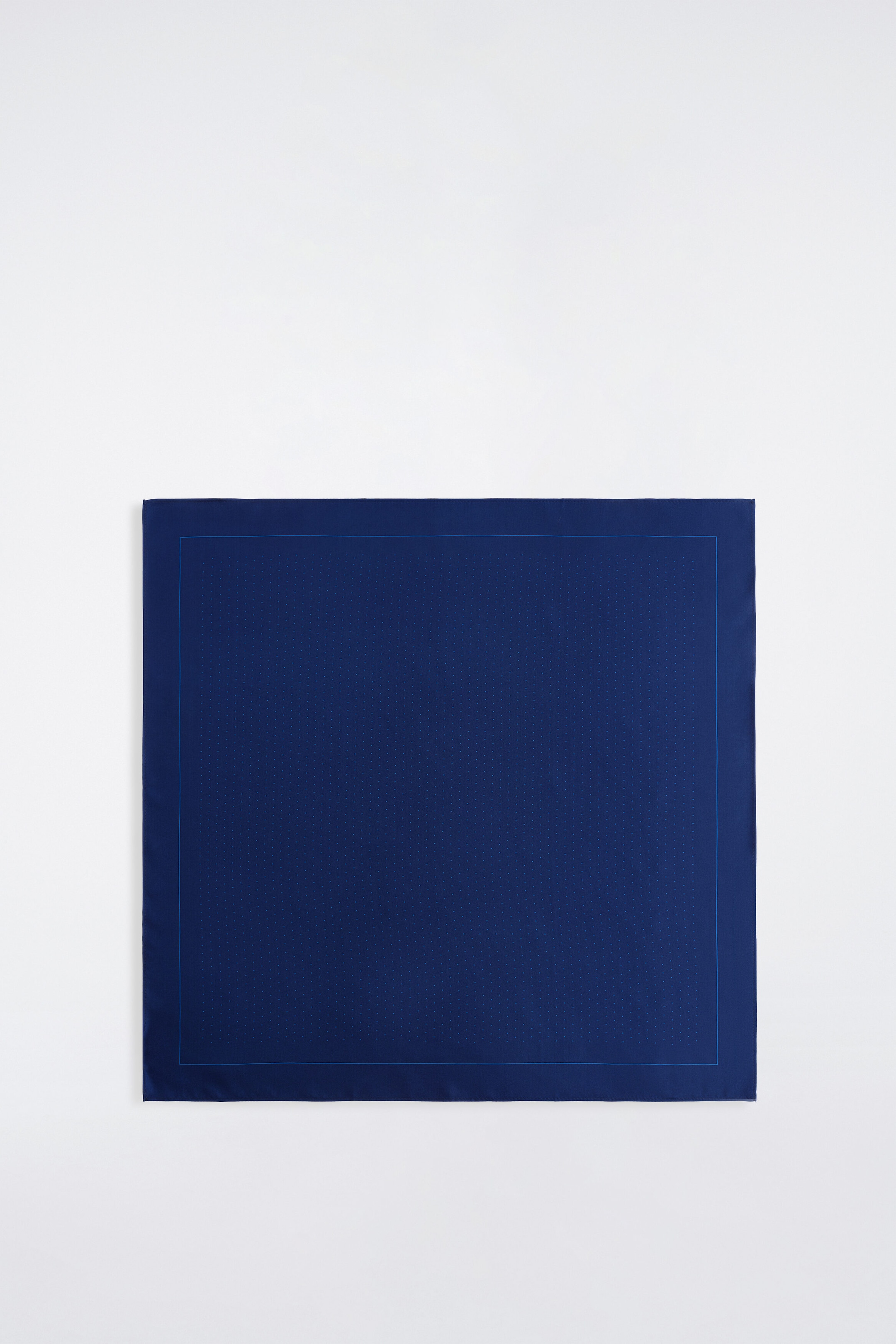 A navy blue silk pocket square is lying flat, facing forward, showcasing a subtle light blue micro-polka-dot pattern. The pattern is framed by a thin light blue line and a solid navy blue outer border.