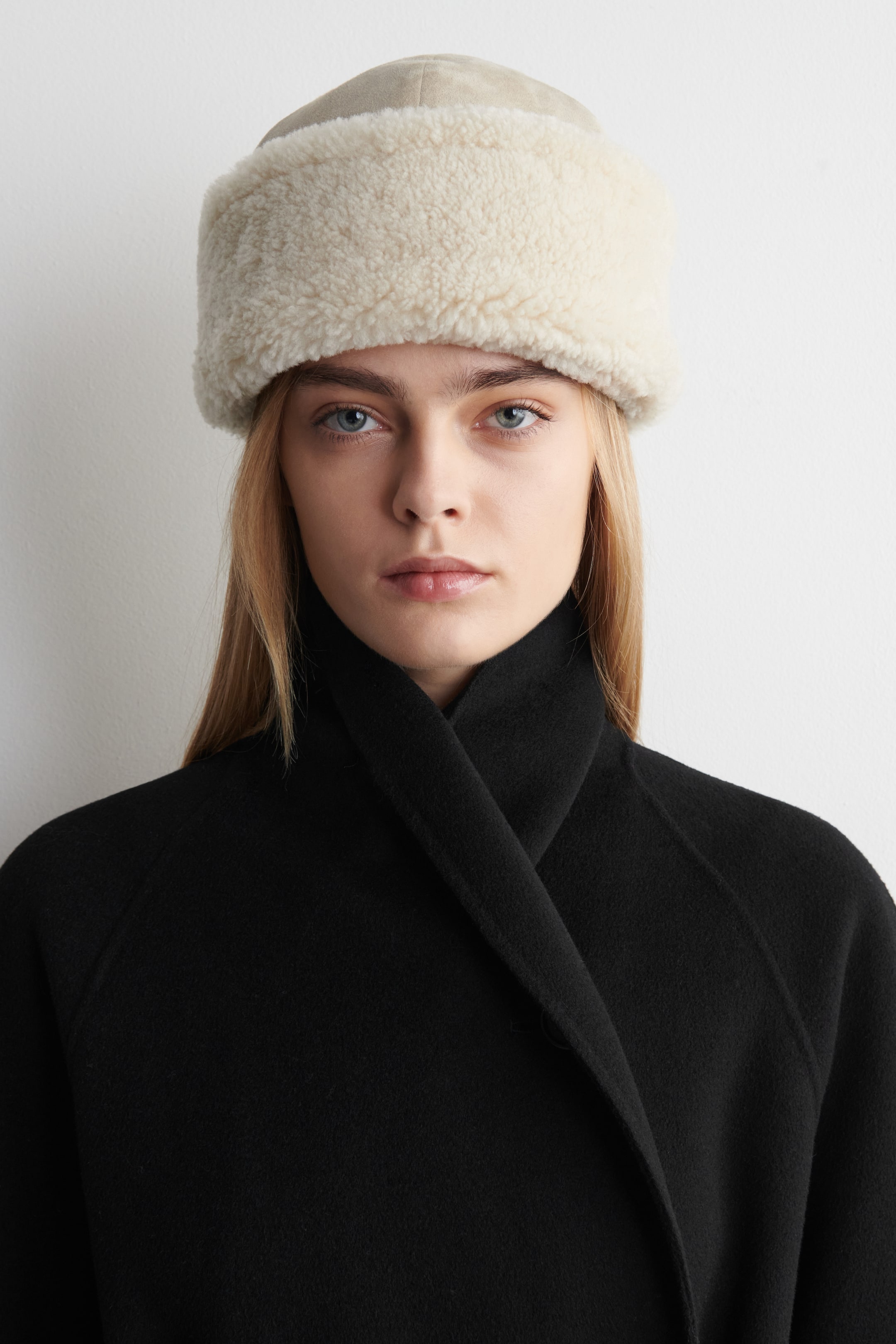 Visualizza l'immagine ingrandita: Un cappello con cupola in suede beige chiaro e un’ampia tesa in shearling color crema. È indossato rivolto in avanti, con la morbida tesa che copre la fronte e le orecchie.