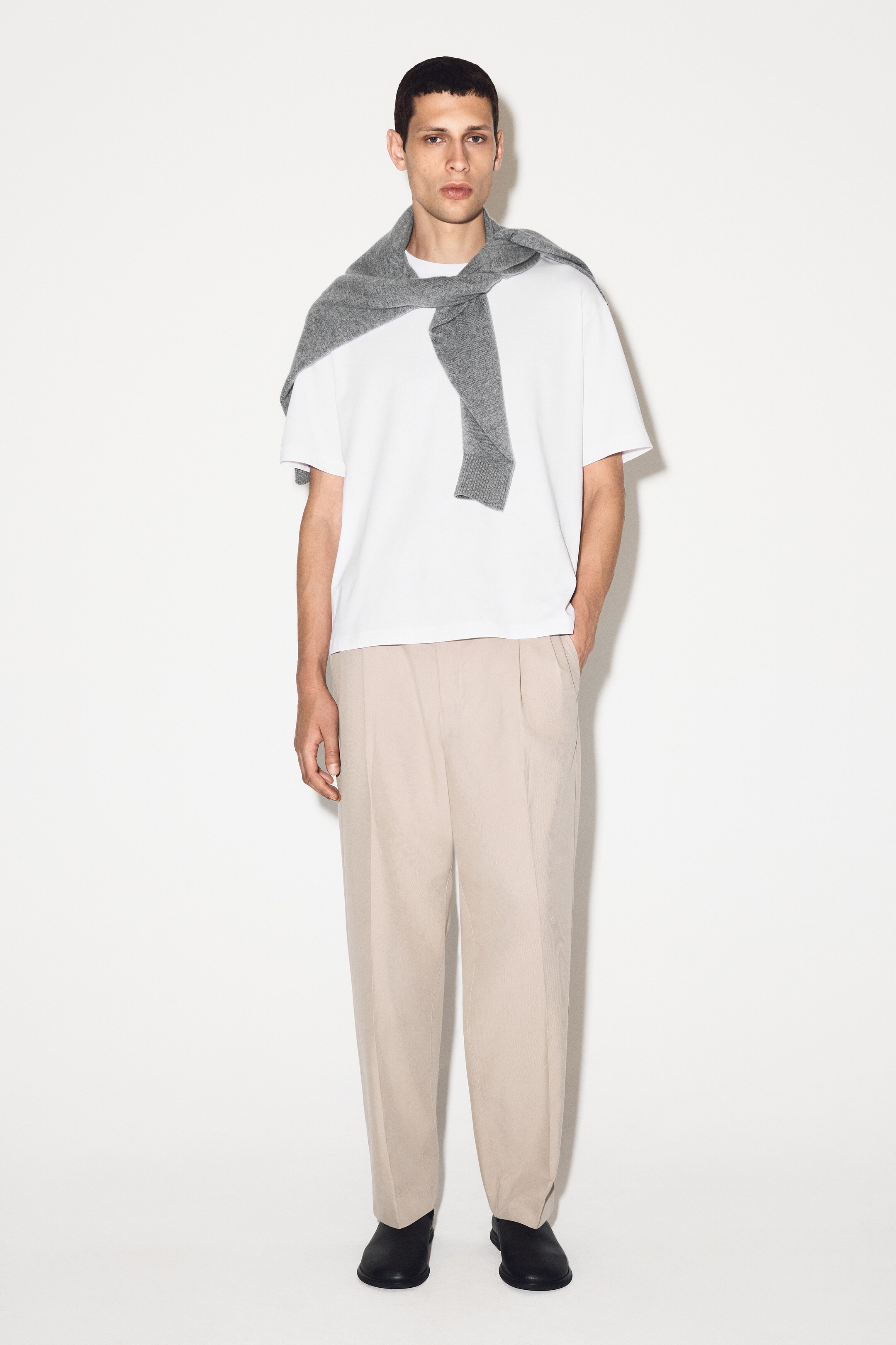 Agrandir l'image: Un T-shirt blanc à coupe décontractée est présenté sur un mannequin de face, avec un col rond et des manches courtes. Un pull gris est drapé sur ses épaules, obscurcissant partiellement les coutures des épaules tombantes.