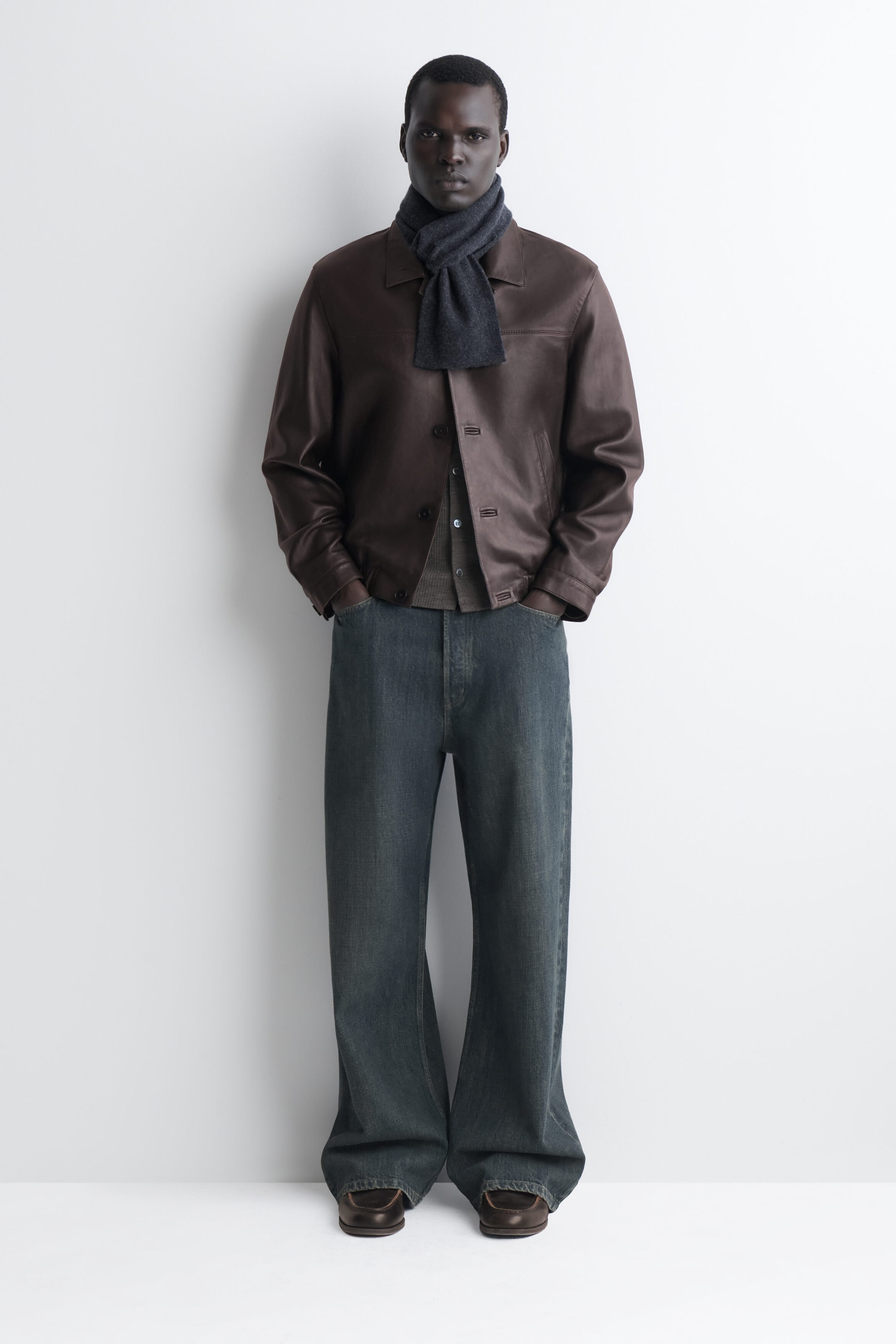 The dark gray cashmere pull-through scarf is shown from the front, wrapping snugly around the neck. One end of the scarf is threaded through a loop on the other side, draping neatly over the collar of a brown leather jacket. The dark gray cashmere pull-through scarf is shown from the front, wrapping snugly around the neck. One end of the scarf is threaded through a loop on the other side, draping neatly over the collar of a brown leather jacket.