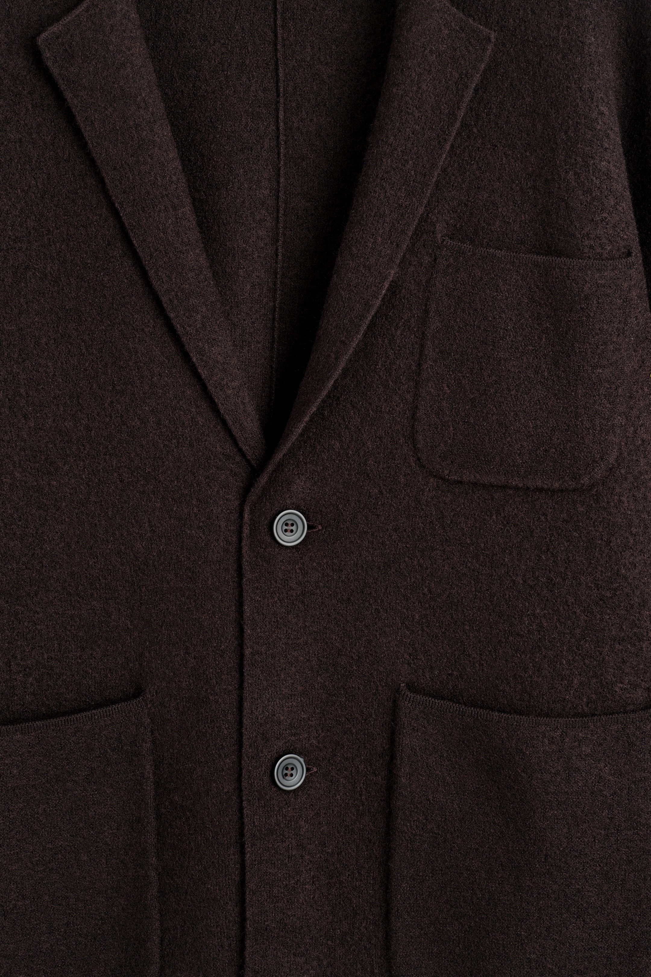 Größeres Bild ansehen: Dieser dunkelbraune Blazer wird von vorne präsentiert, mit einem strukturierten, gekochten Merinowollstoff. Er ist mit klassischen Kerbrevers, zwei sichtbaren tonalen Knöpfen und zwei großen aufgesetzten Vordertaschen gestaltet.