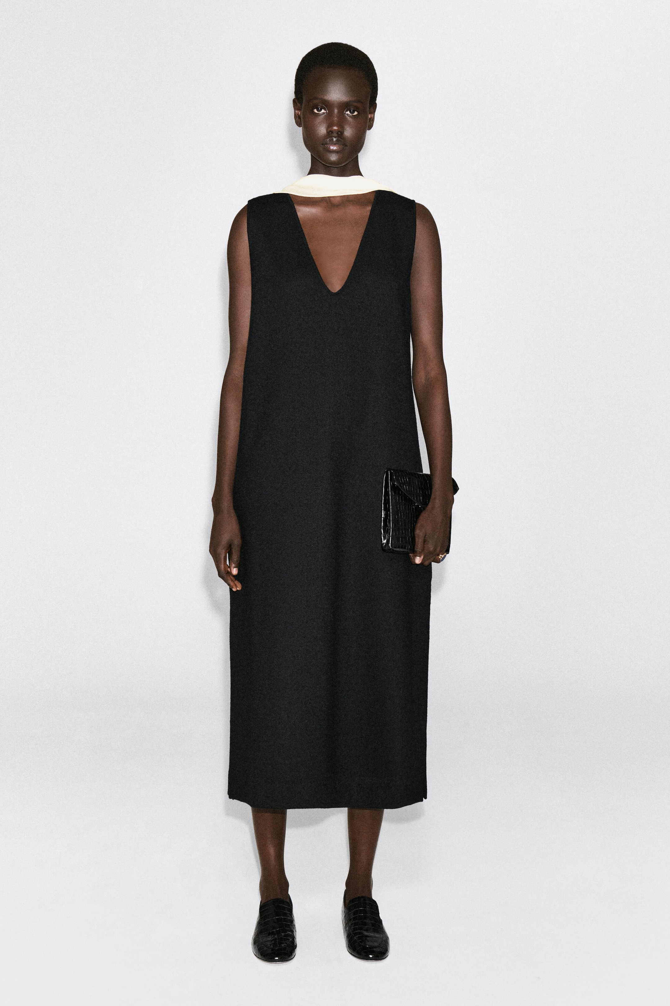 The boiled wool-blend V-neck midi dress is shown from the front, featuring a sleeveless, relaxed silhouette with a deep V-neckline. The dress falls to a midi length and is styled with a cream-colored neckband accessory layered underneath to highlight its minimalist design. The boiled wool-blend V-neck midi dress is shown from the front, featuring a sleeveless, relaxed silhouette with a deep V-neckline. The dress falls to a midi length and is styled with a cream-colored neckband accessory layered underneath to highlight its minimalist design.