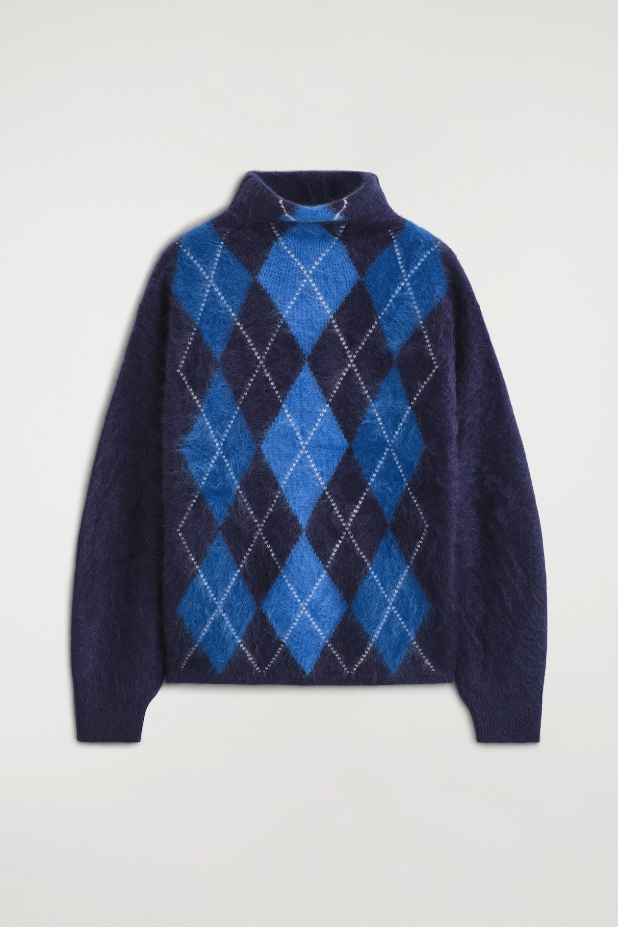 The Argyle Brushed Pure Cashmere Funnel-Neck Jumper is shown front-facing, featuring a soft, brushed texture with a classic navy and bright blue argyle pattern across the torso. This long-sleeved jumper features a high funnel neck, ribbed cuffs, and a straight hem.