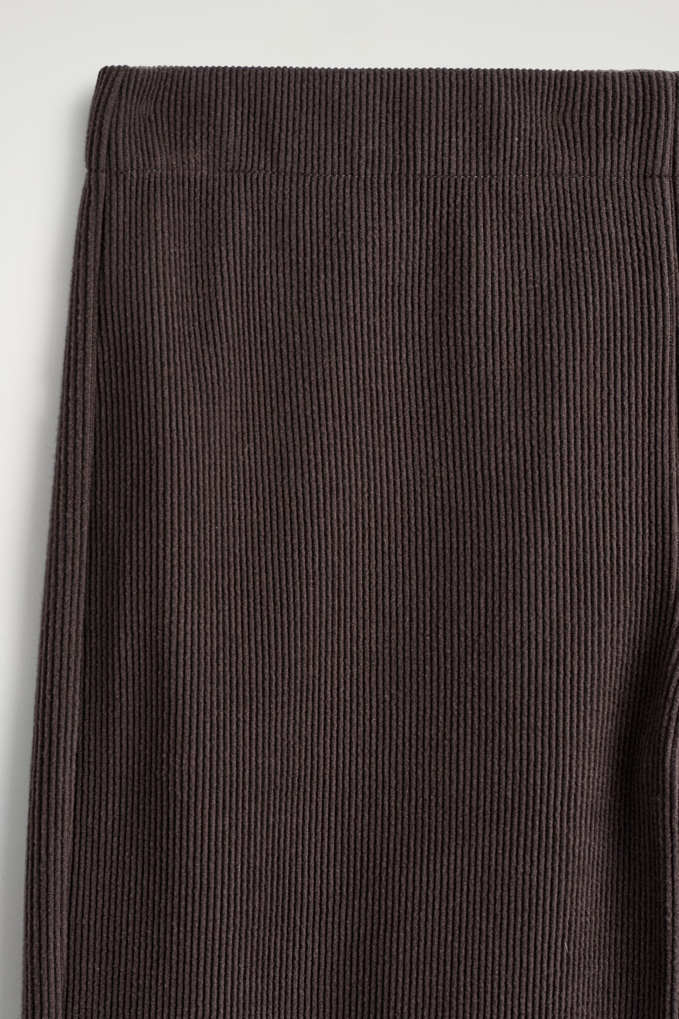 Ver imagen más grande: Los pantalones de pana de color marrón oscuro presentan una textura finamente acanalada, con una cinturilla elástica visible en la parte superior.