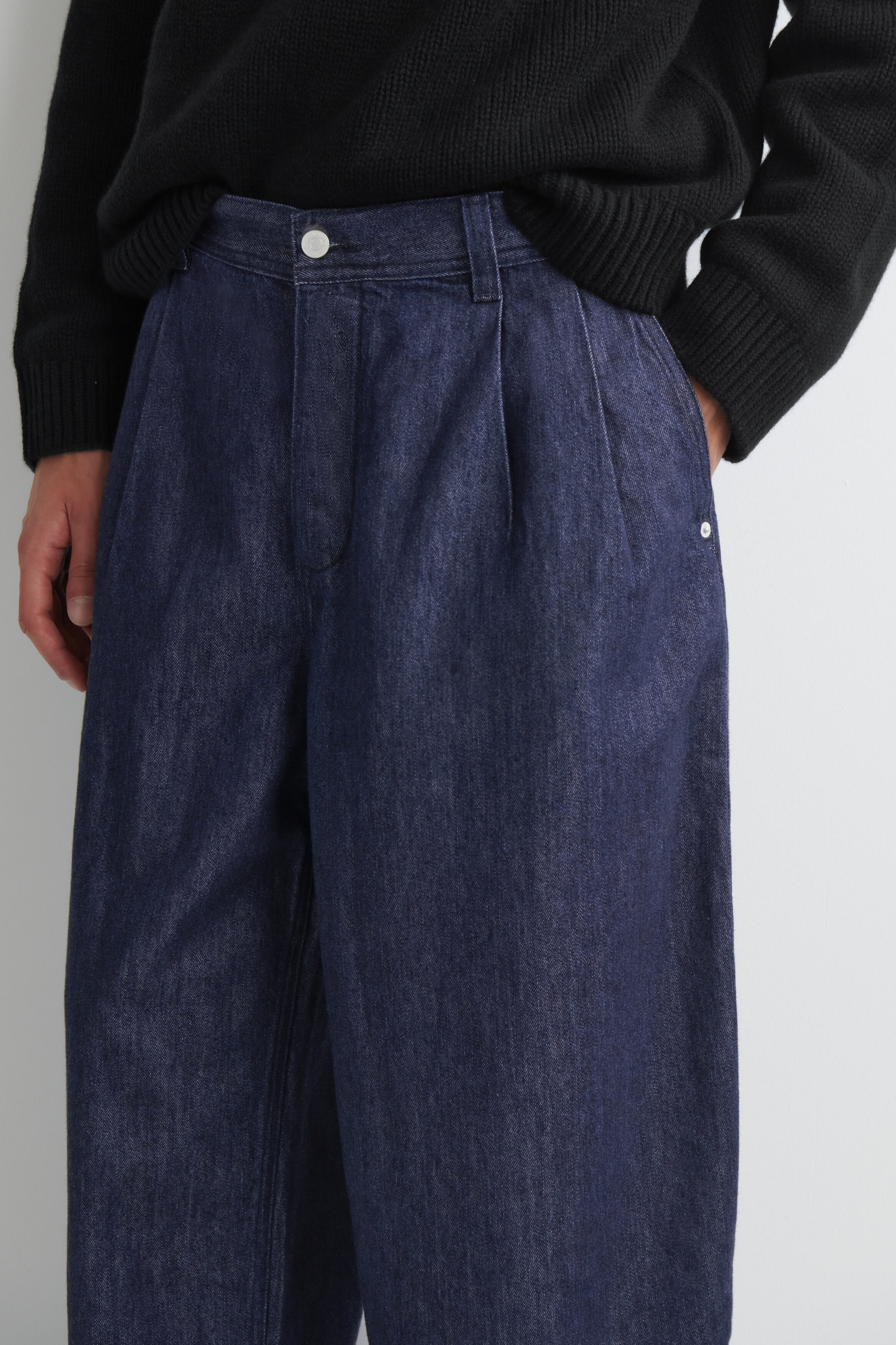 Ce pantalon barrel en denim plissé à coupe décontractée est présenté de face, mettant en valeur un délavage indigo foncé, une taille haute avec des plis structurés sur le devant et une fermeture à bouton. Le pantalon affiche une silhouette ample à jambe large et est porté avec un pull noir en maille côtelée rentré dans la ceinture. Ce pantalon barrel en denim plissé à coupe décontractée est présenté de face, mettant en valeur un délavage indigo foncé, une taille haute avec des plis structurés sur le devant et une fermeture à bouton. Le pantalon affiche une silhouette ample à jambe large et est porté avec un pull noir en maille côtelée rentré dans la ceinture.