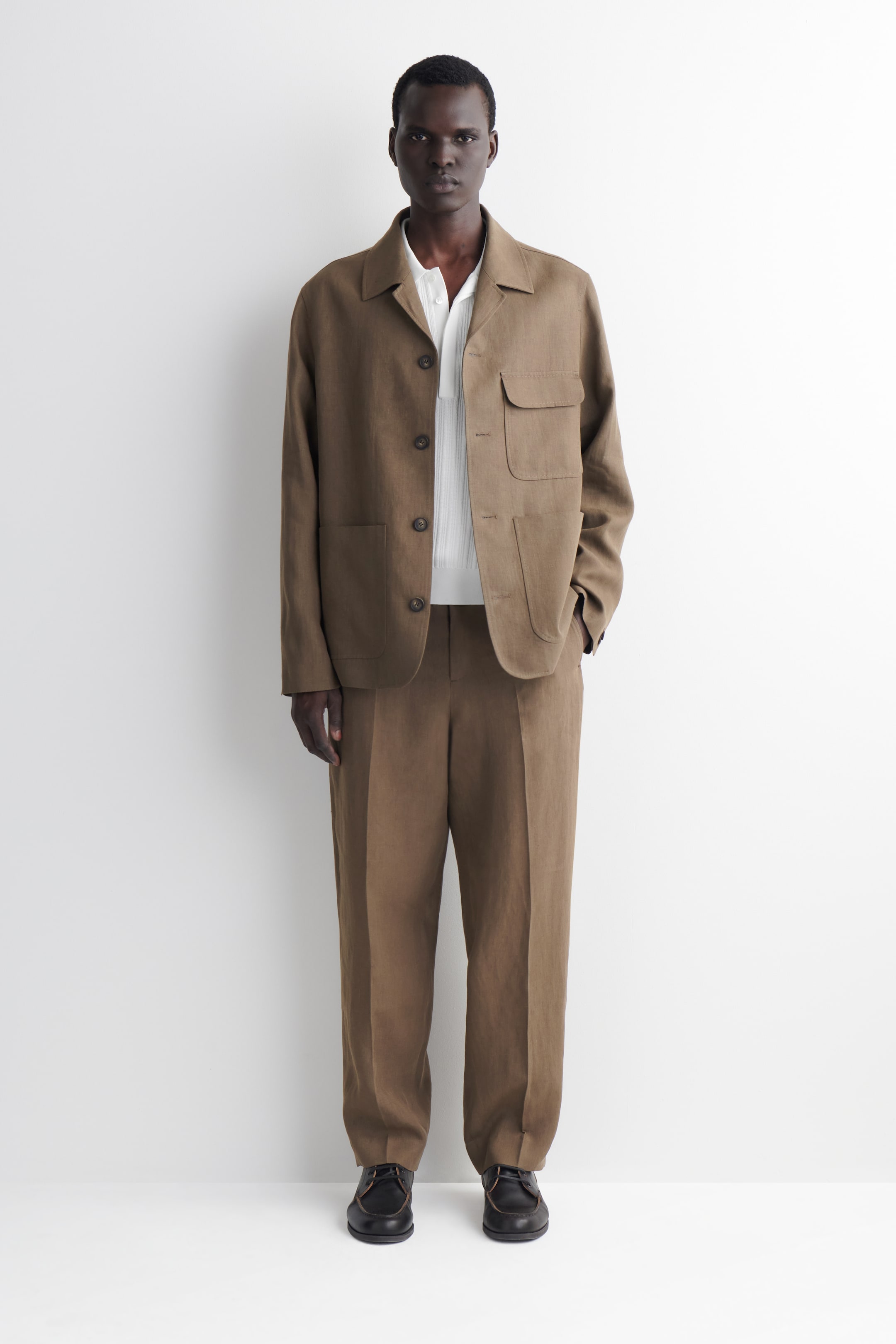 Visualizza l'immagine ingrandita: Un blazer in lino color kaki brunito e pantaloni coordinati sono presentati su una modella. Il blazer destrutturato presenta una chiusura frontale con bottoni marroni, un colletto a camicia e tre grandi tasche applicate, indossato sopra una camicia bianca con colletto.