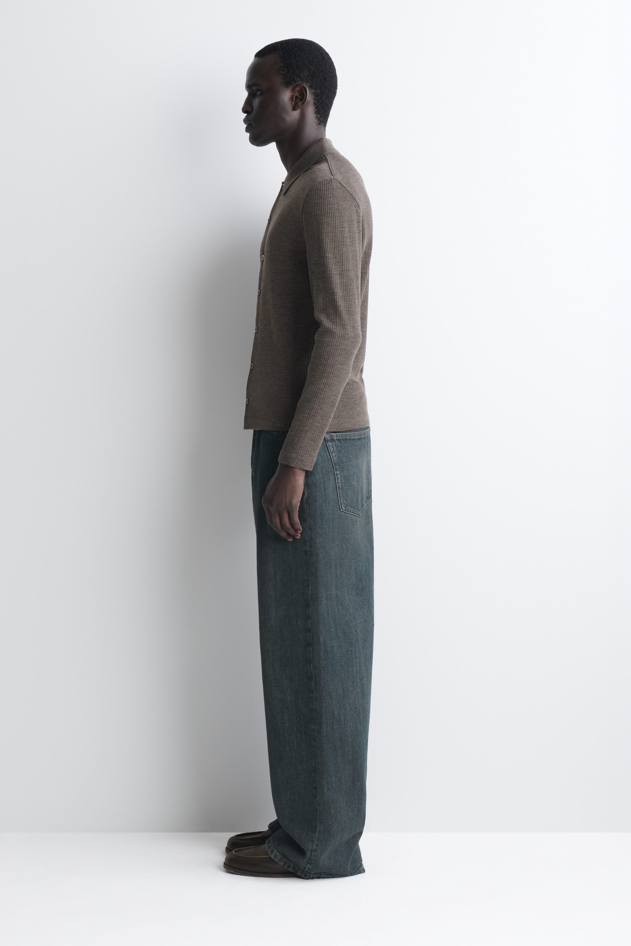 Das schmale Wollhemd mit Rippstruktur in Taupe-Braun wird in der Seitenansicht nach links gezeigt und betont so die eng anliegende Silhouette und die feine Rippstruktur. Es verfügt über einen klassischen Kragen, lange Ärmel und eine durchgehende Knopfleiste; der gerade Saum fällt unordentlich über die weit geschnittene Jeans. Das schmale Wollhemd mit Rippstruktur in Taupe-Braun wird in der Seitenansicht nach links gezeigt und betont so die eng anliegende Silhouette und die feine Rippstruktur. Es verfügt über einen klassischen Kragen, lange Ärmel und eine durchgehende Knopfleiste; der gerade Saum fällt unordentlich über die weit geschnittene Jeans.