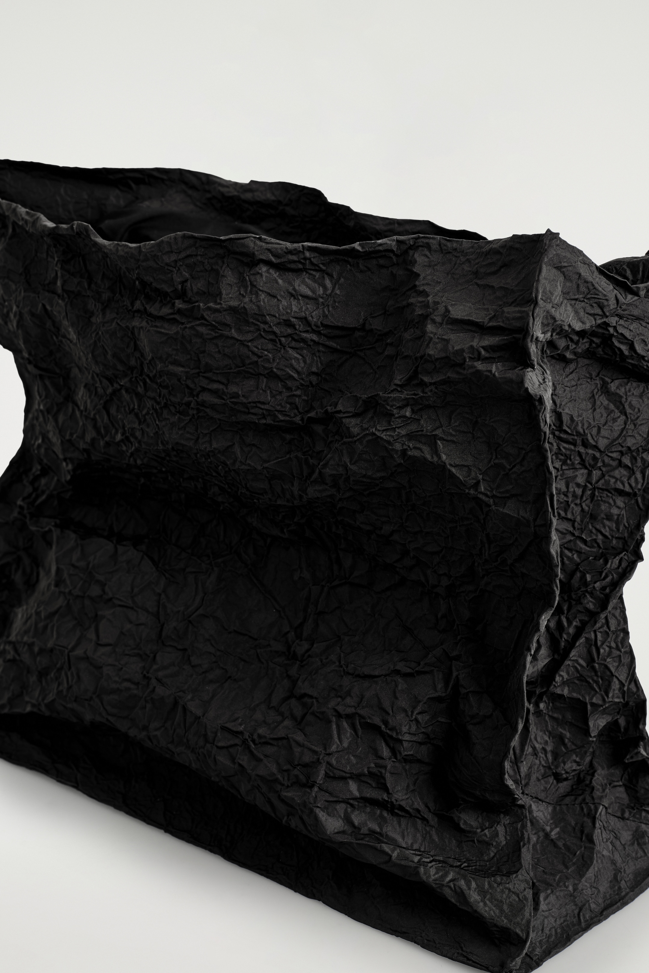 Visualizza immagine più grande: Una clutch nera oversize è presentata con l'apertura superiore rivolta verso l'osservatore. Presenta una texture di tessuto fortemente stropicciata, creando una silhouette esagerata e non strutturata.