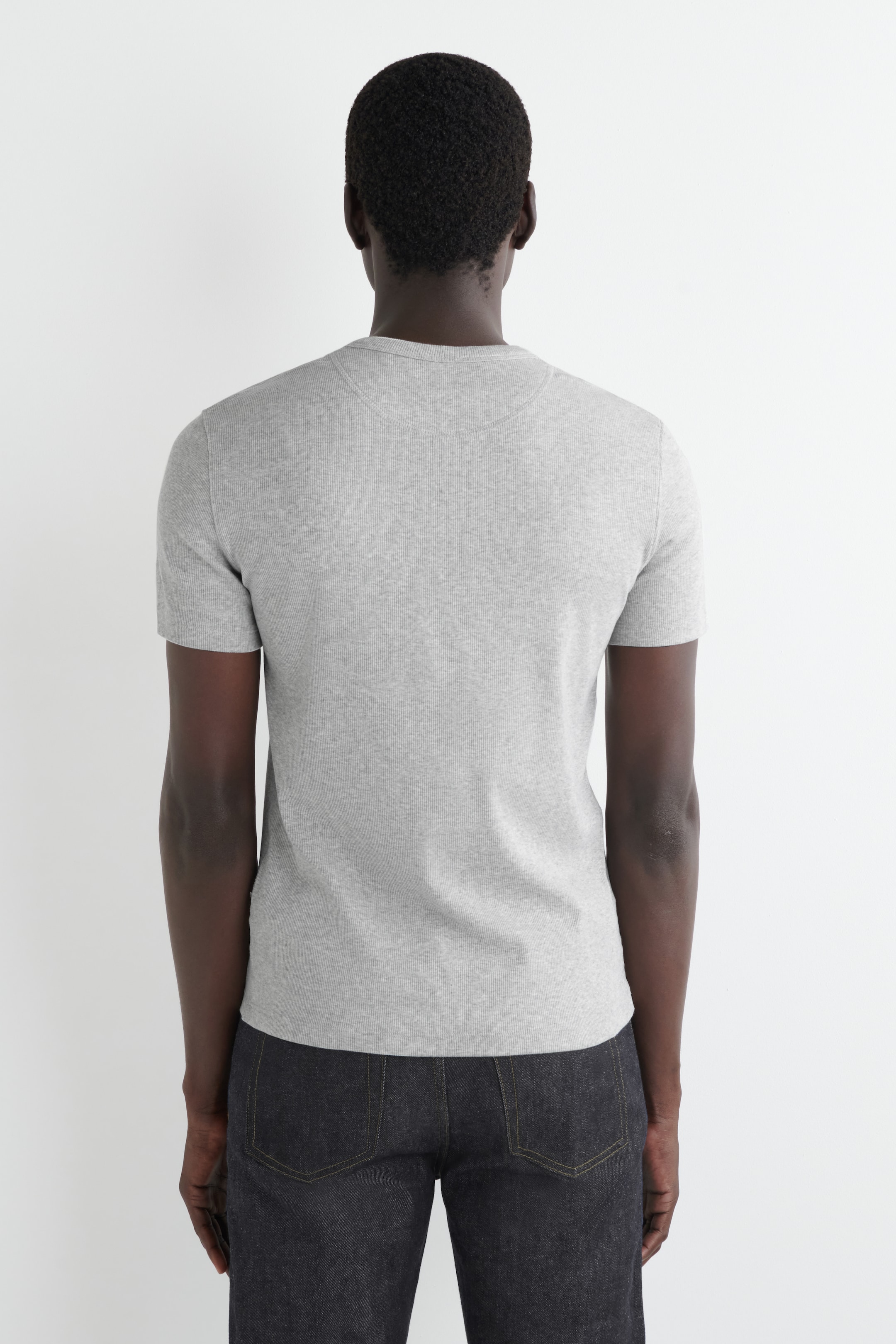View larger image: A grey short-sleeved top is being presented from the back, featuring a ribbed knit texture. The top is designed with a crew neck and short sleeves.