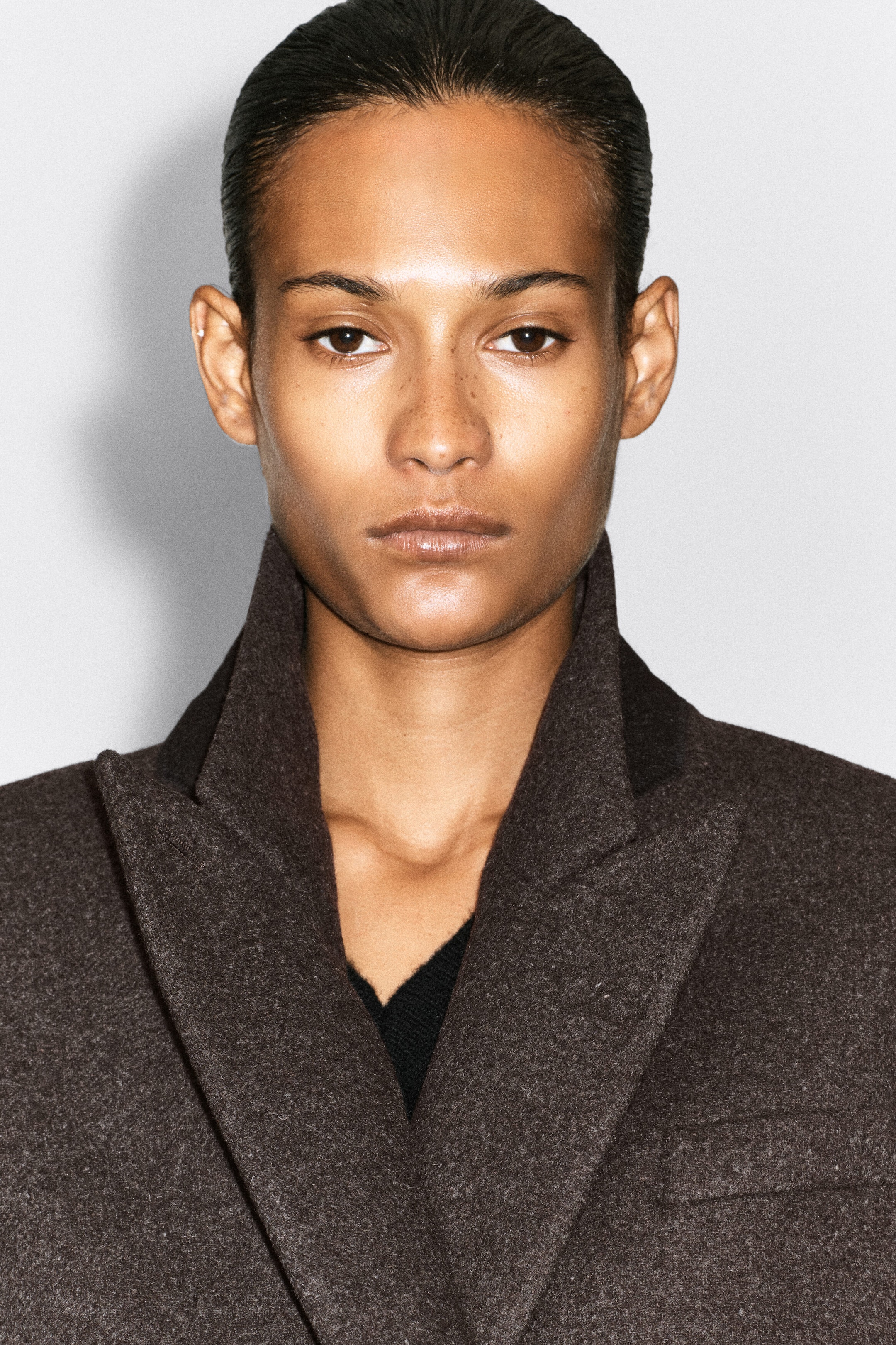The model is wearing a dark brown boiled wool blend blazer, featuring wide notch lapels and a textured finish. The blazer is layered over a black knit top. The model is wearing a dark brown boiled wool blend blazer, featuring wide notch lapels and a textured finish. The blazer is layered over a black knit top.