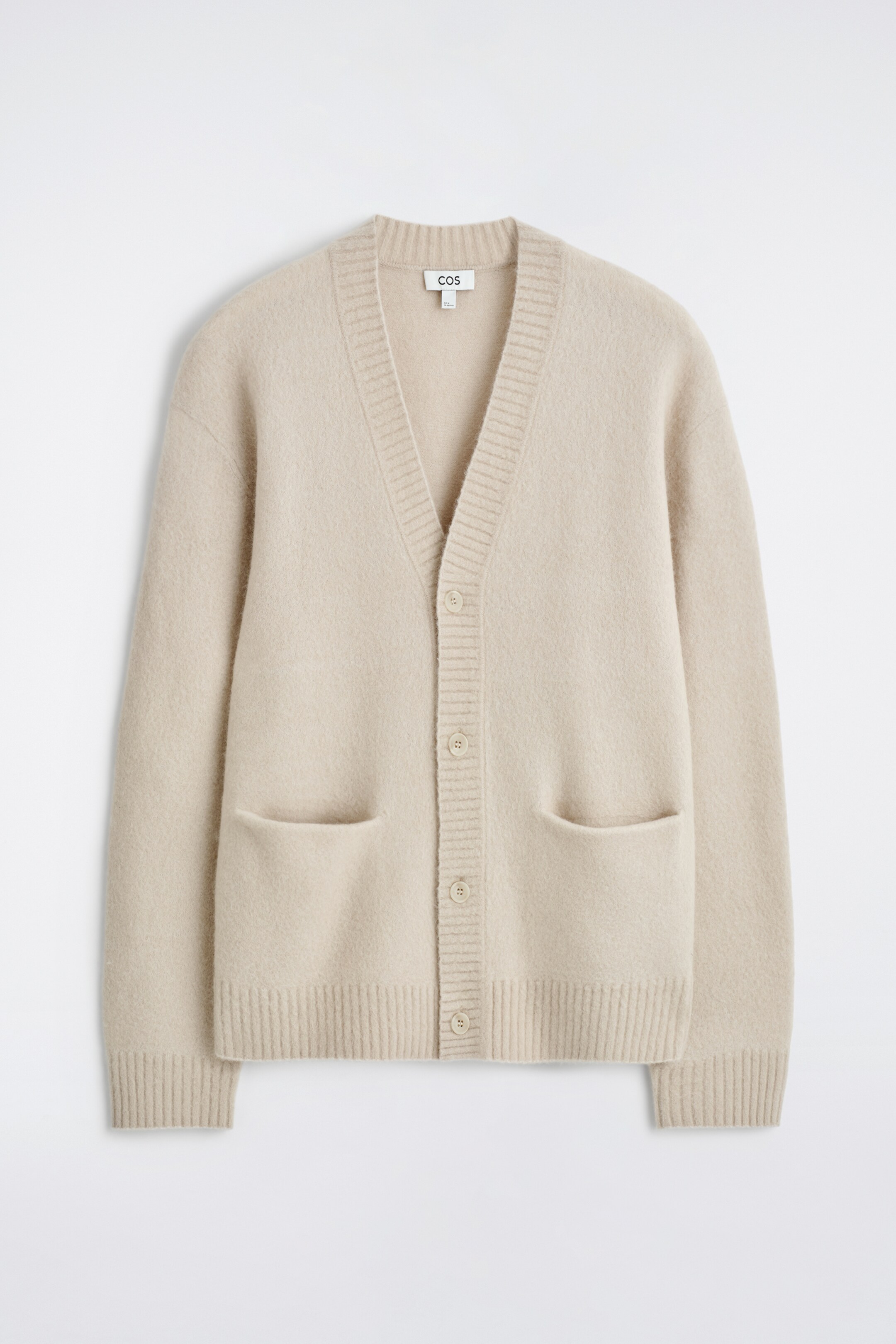 Ver imagen más grande: Se presenta un cárdigan beige claro de frente, mostrando una textura cepillada. Está diseñado con una solapa de cuello en V acanalada, un cierre frontal de botones, dos bolsillos de parche y puños y dobladillo acanalados.