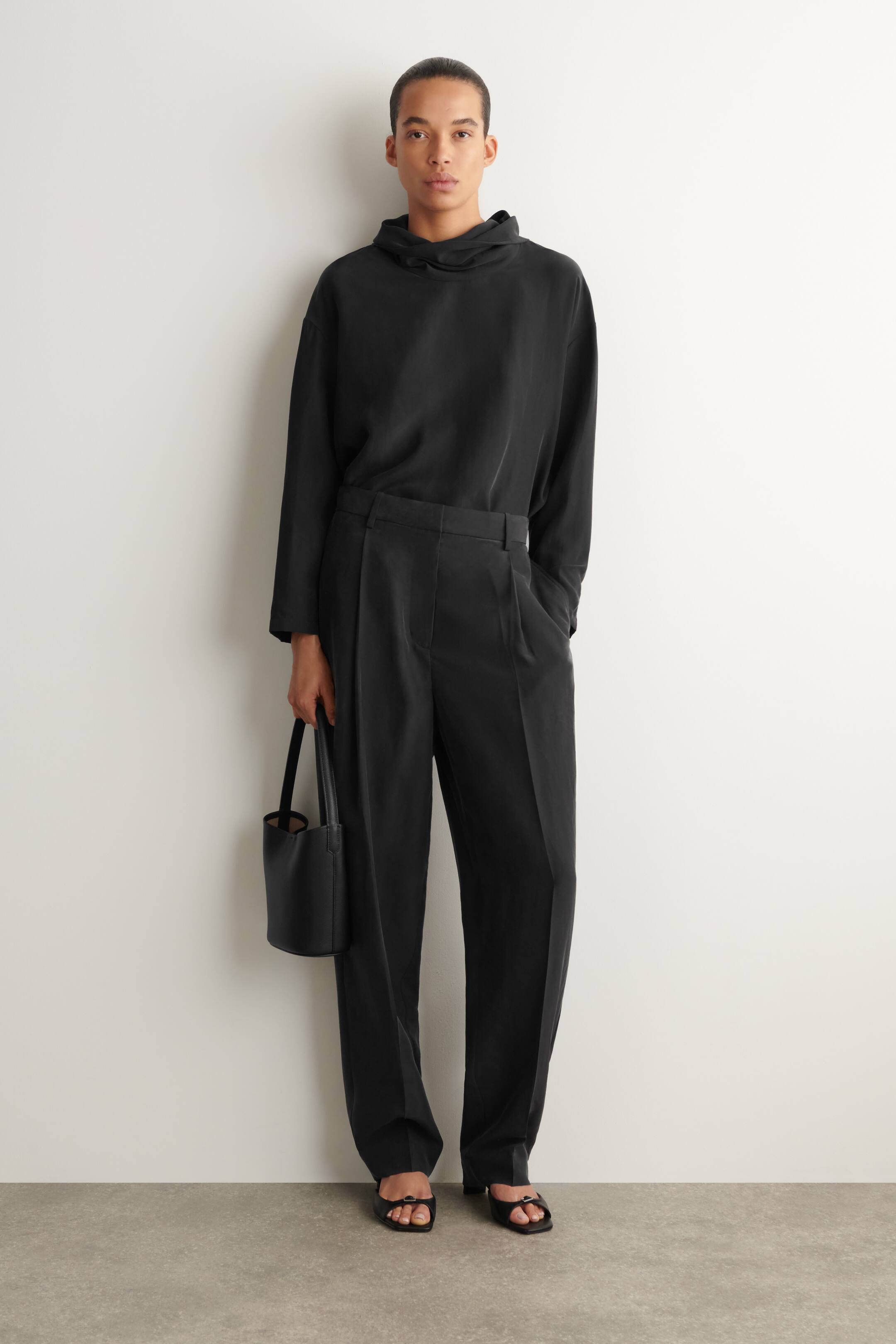 Agrandir l'image: Pantalon noir à jambes droites offrant une coupe décontractée avec une ceinture plate et un pli avant unique. Le tissu présente un drapé doux et une texture subtilement froissée.