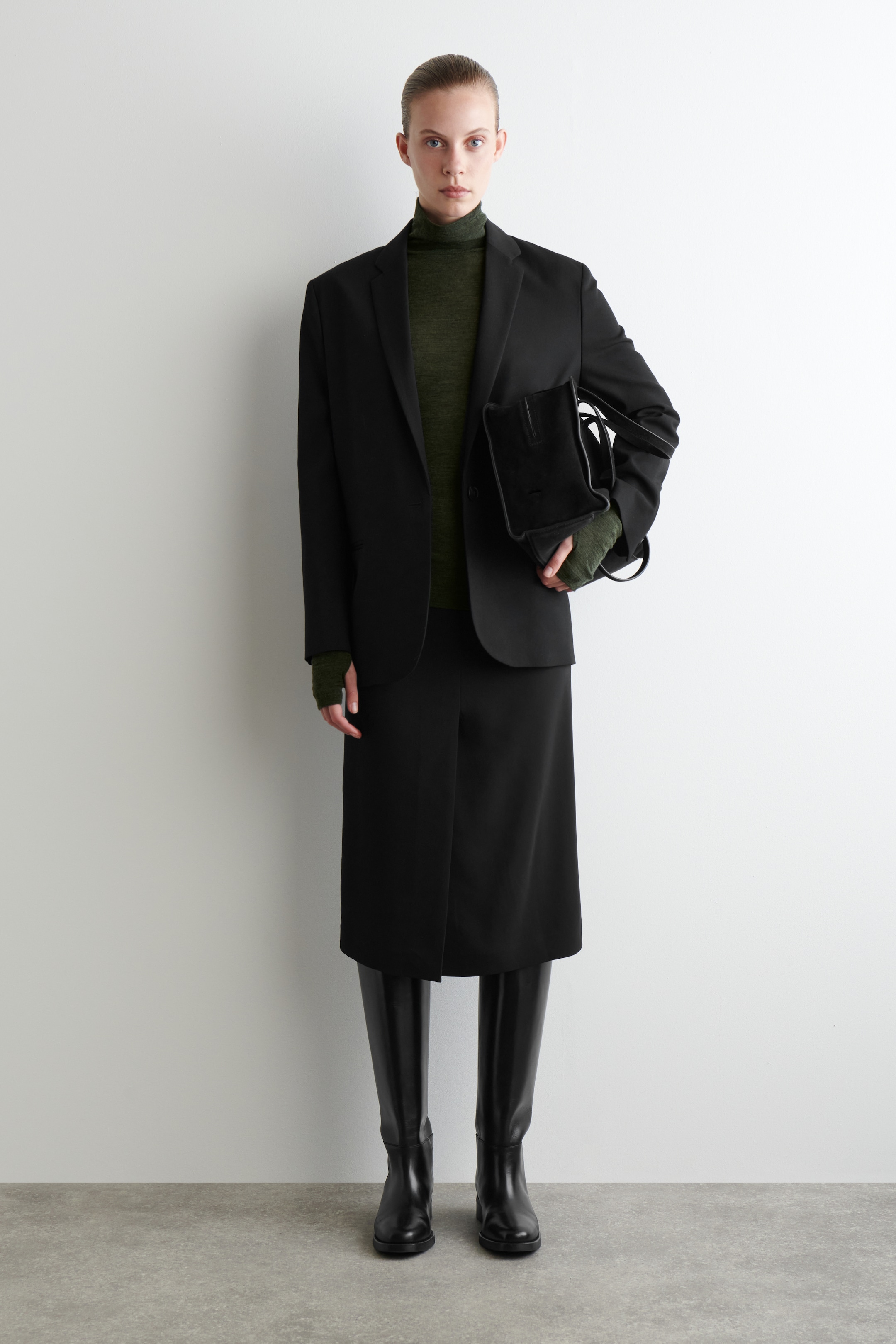 Grösseres Bild ansehen: Ein schwarzer einreihiger Blazer mit Kerbrevers wird frontseitig getragen, über einem olivgrünen Feinstrick-Rollkragenpullover. Er wird mit einem schwarzen Midirock und schwarzen kniehohen Stiefeln gestylt, während eine schwarze strukturierte Handtasche gehalten wird.