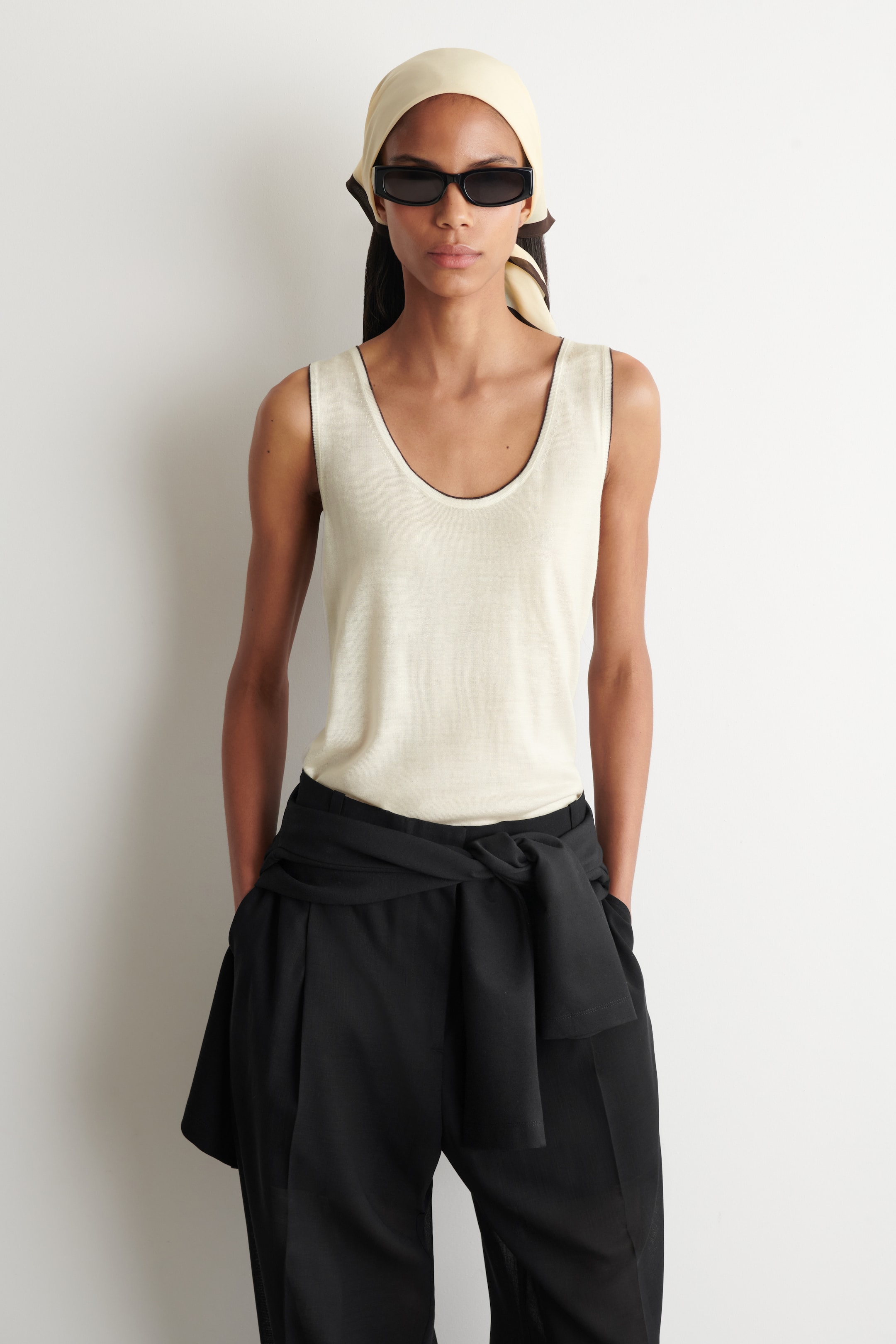 Agrandir l'image: Les pantalons noirs sont présentés de face avec une coupe ample et jambes larges, dotés de plis marqués à l'avant et d'une taille haute. Un vêtement noir assorti est noué autour de la taille, formant un nœud à l'avant.