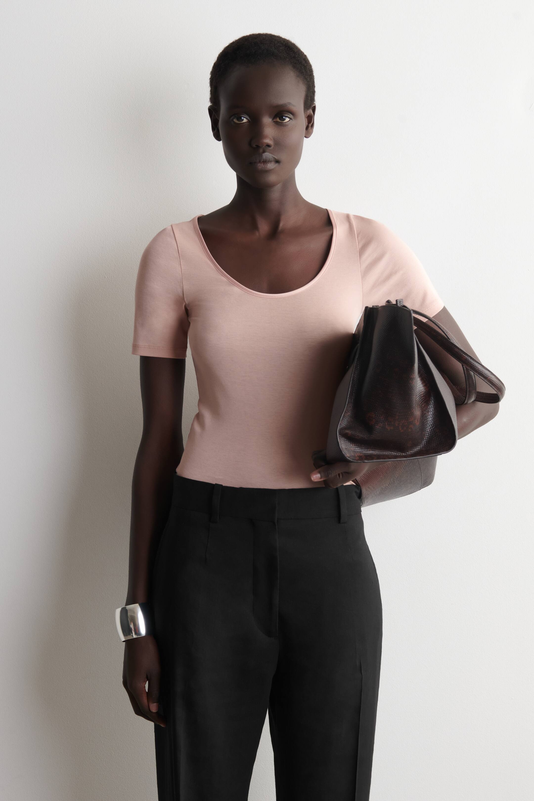 Agrandir l'image: Un haut à manches courtes rose clair, doté d'un col rond et d'une coupe ajustée, est porté rentré dans un pantalon noir. Le pantalon présente une coupe droite et des passants de ceinture visibles.