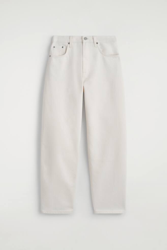 Un jean en denim blanc cassé est présenté DE FACE, à plat, avec une ceinture dotée de passants et une fermeture à bouton unique. Le jean affiche des jambes en forme de tonneau qui semblent incurvées et larges, avec des poches avant en forme de pelle et une poche à monnaie. - 1