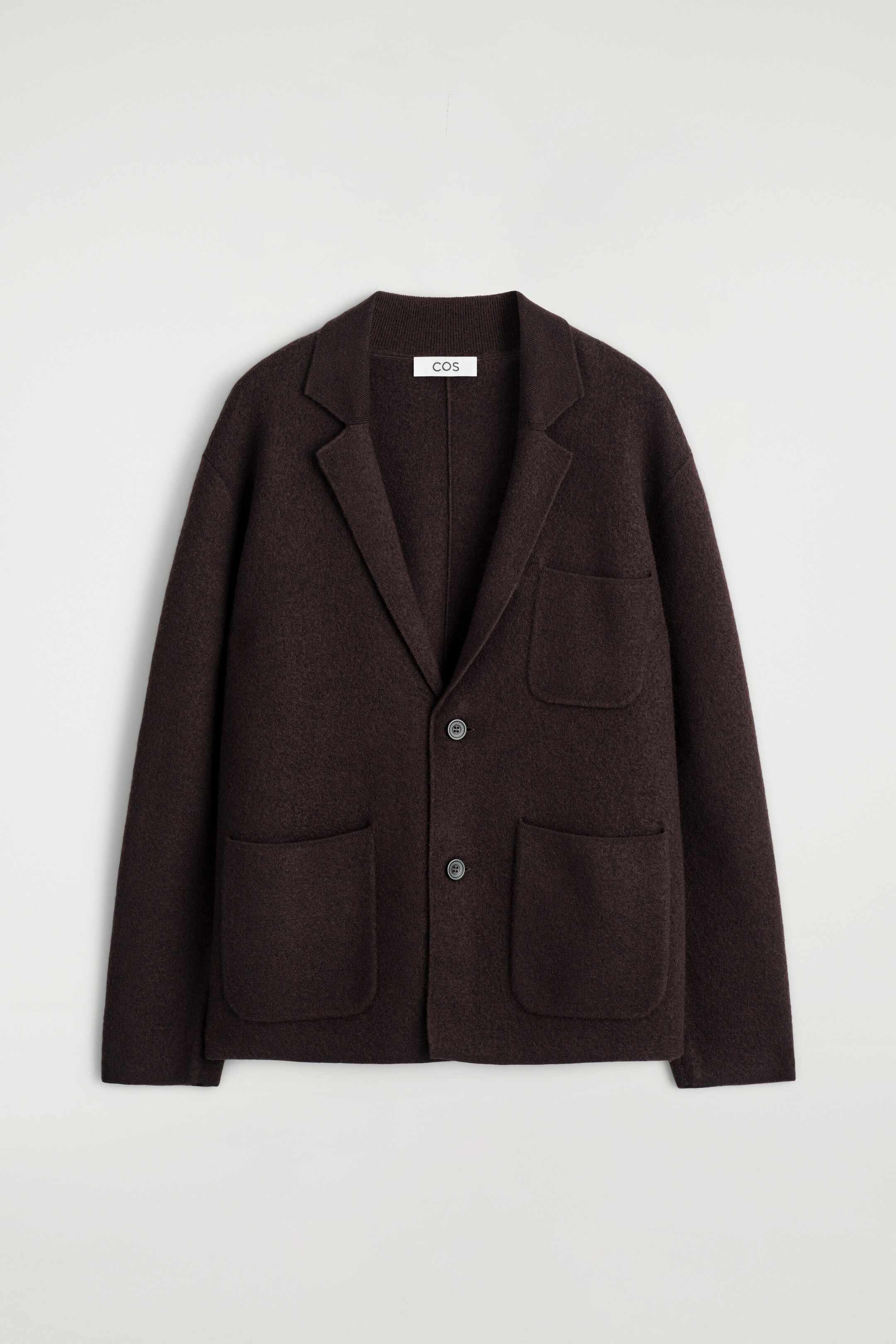 Ver imagem maior: Um blazer castanho escuro está a ser apresentado como FRENTE, apresentando um tecido texturizado de lã merino fervida. É desenhado com lapelas clássicas em bico, dois botões tonais para fecho e três bolsos frontais de patch, incluindo um no peito e dois maiores na parte inferior.