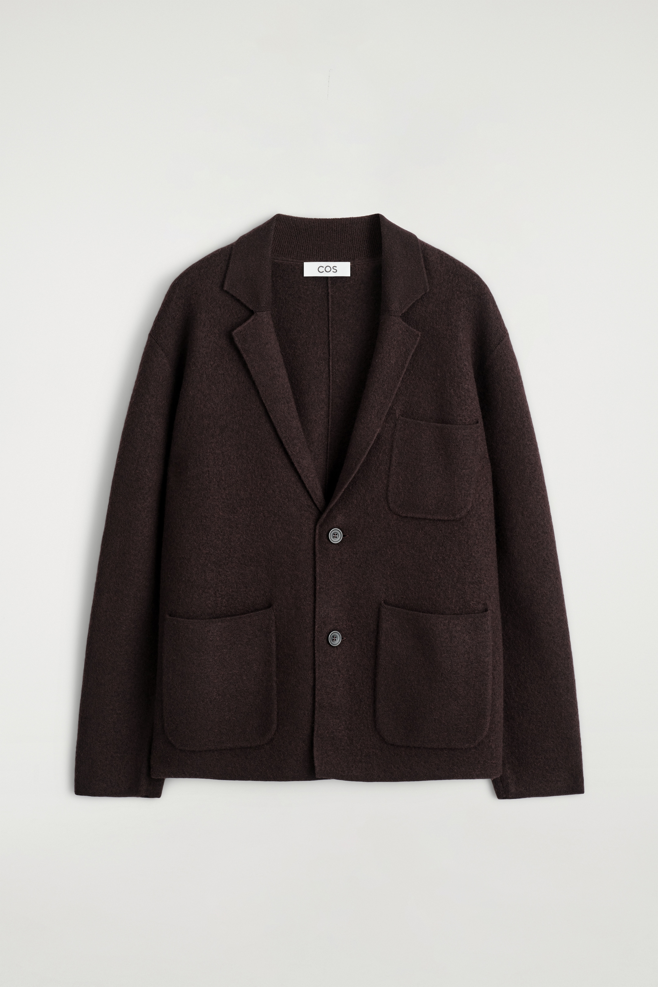 Größeres Bild ansehen: Ein dunkelbrauner Blazer wird als FRONT präsentiert, mit einem strukturierten, gekochten Merinowollstoff. Er ist mit klassischen Kerbrevers, zwei tonalen Knöpfen zum Schließen und drei aufgesetzten Taschen vorne gestaltet, darunter eine auf der Brust und zwei größere unten.