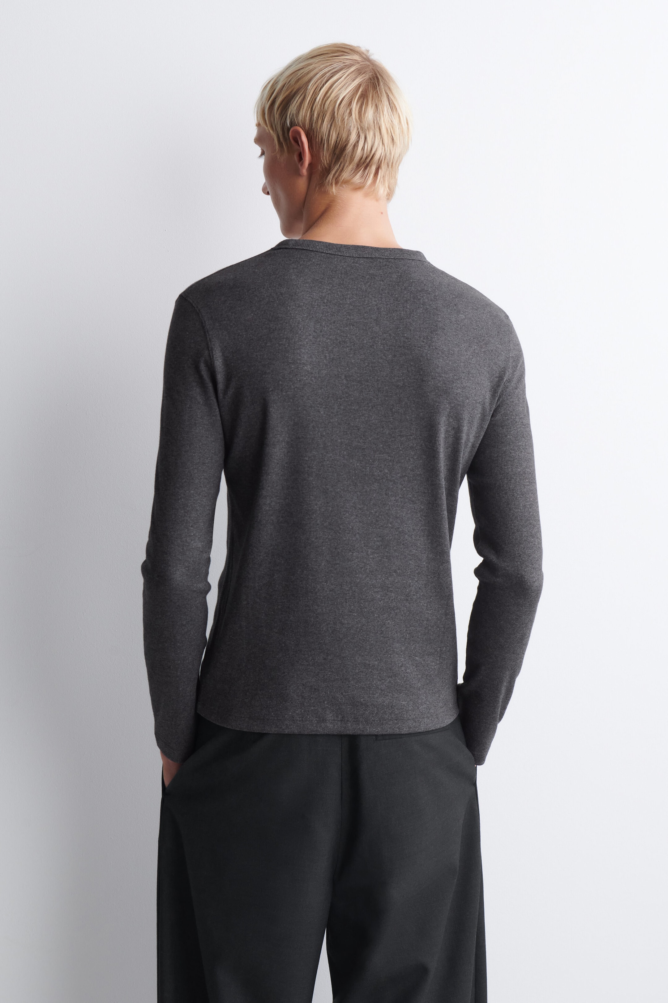 A dark gray long-sleeve T-shirt is shown from the back, featuring a classic crew neck and a straight hem. The top fits smoothly across the shoulders and ends just below the waistline of black trousers.