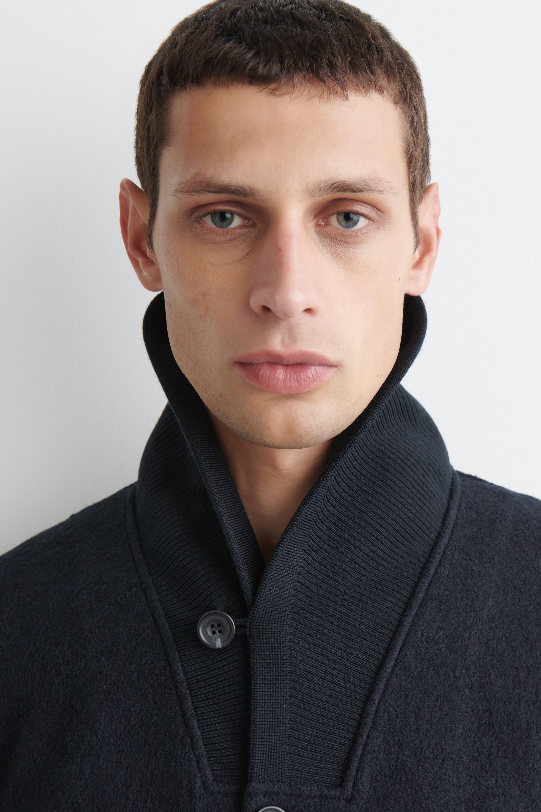 The boiled wool shawl-collar jacket is shown in a close-up, front-facing view, highlighting its textured, dark fabric. The jacket features a high-standing, ribbed shawl collar framing the neck and a single-button fastening at the base. The boiled wool shawl-collar jacket is shown in a close-up, front-facing view, highlighting its textured, dark fabric. The jacket features a high-standing, ribbed shawl collar framing the neck and a single-button fastening at the base.