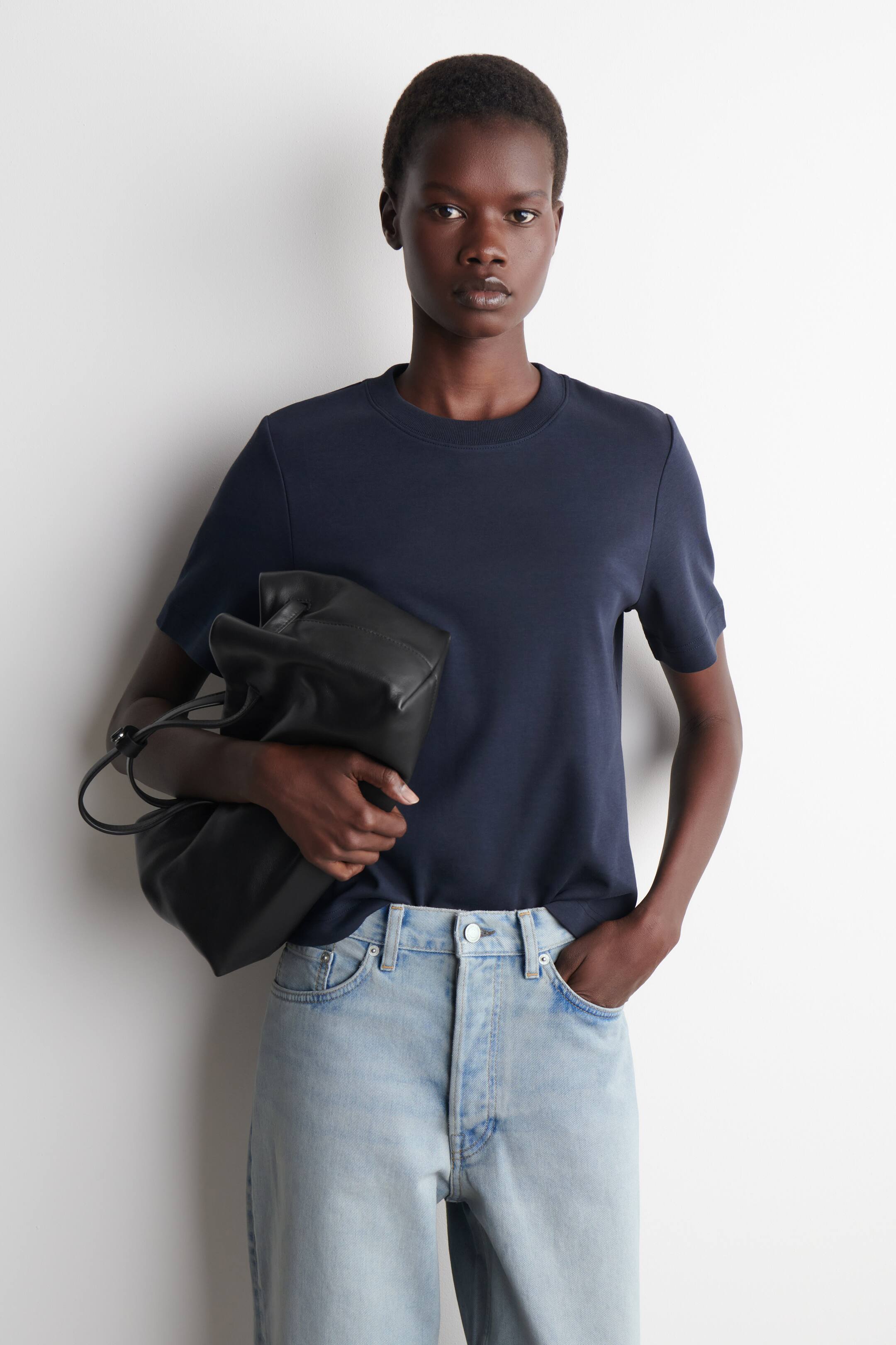 Ver imagen más grande: Se lleva puesta una camiseta de manga corta azul marino, con cuello redondo y un ajuste holgado. Su dobladillo recto está visible, con un lado metido de manera informal.