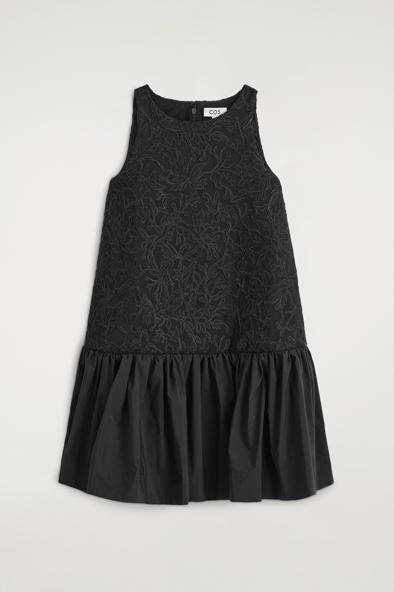 A black sleeveless dress is shown from the front, featuring a textured bodice with intricate tonal floral embroidery and a contrasting gathered poplin skirt that creates a voluminous balloon silhouette.