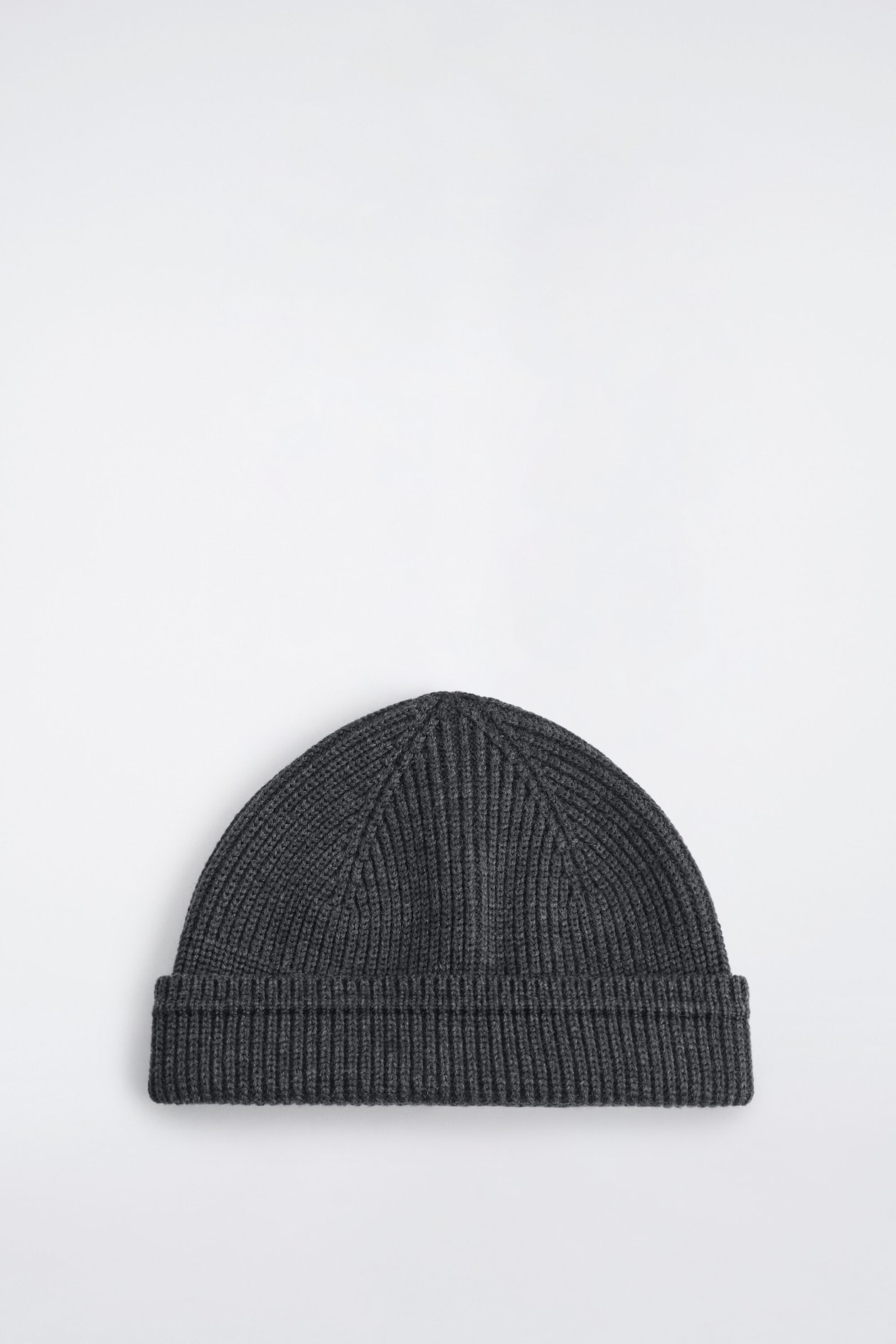 A dark gray ribbed wool-cotton fisherman beanie is laid flat in a front view, showcasing its textured vertical rib knit. The beanie features a thick, folded-up cuff and visible structured seams meeting at the crown.