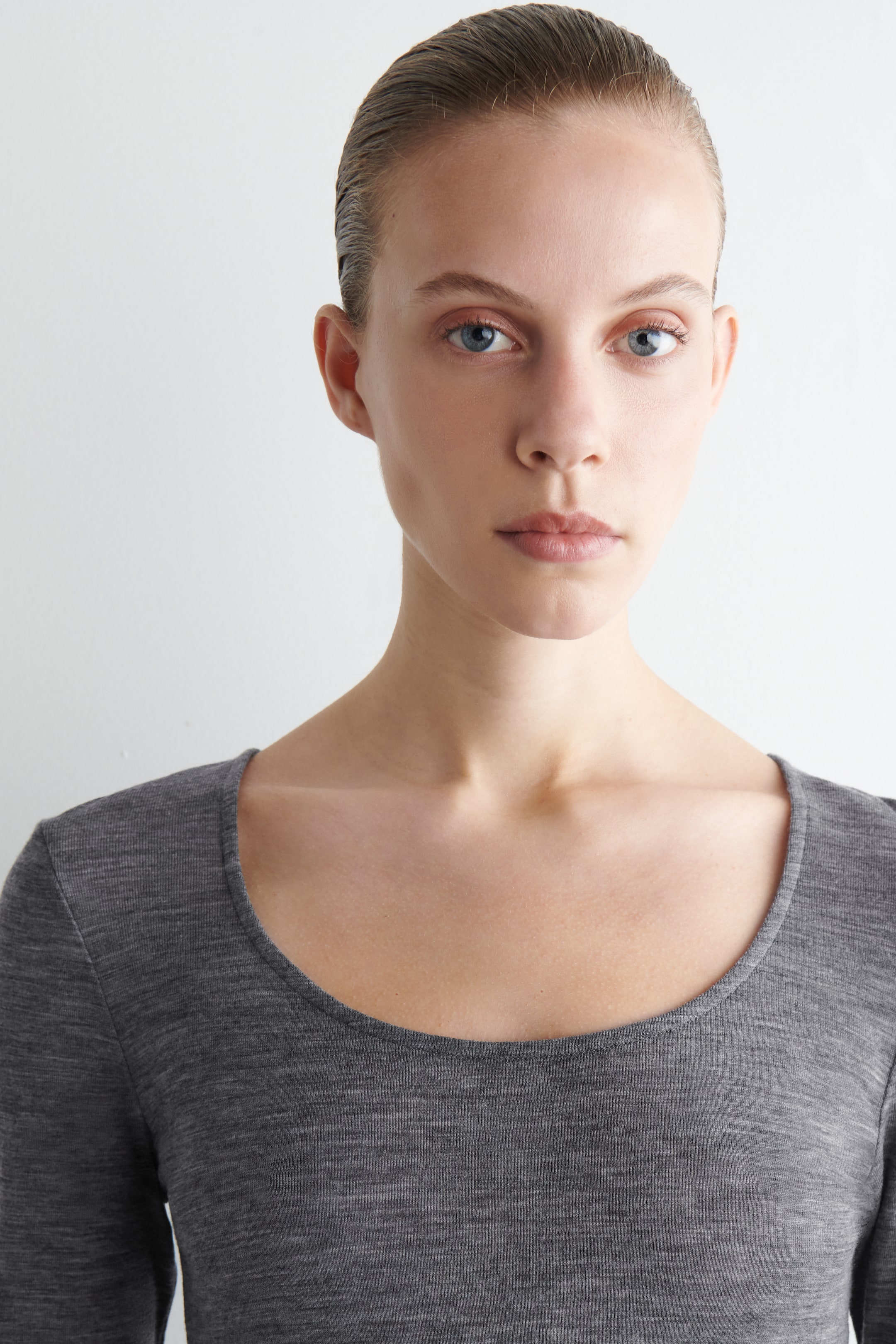 Grösseres Bild ansehen: Ein graues langärmliges Oberteil wird getragen, das einen Rundhalsausschnitt und eine figurbetonte Silhouette in einem feinen Strickstoff aufweist.