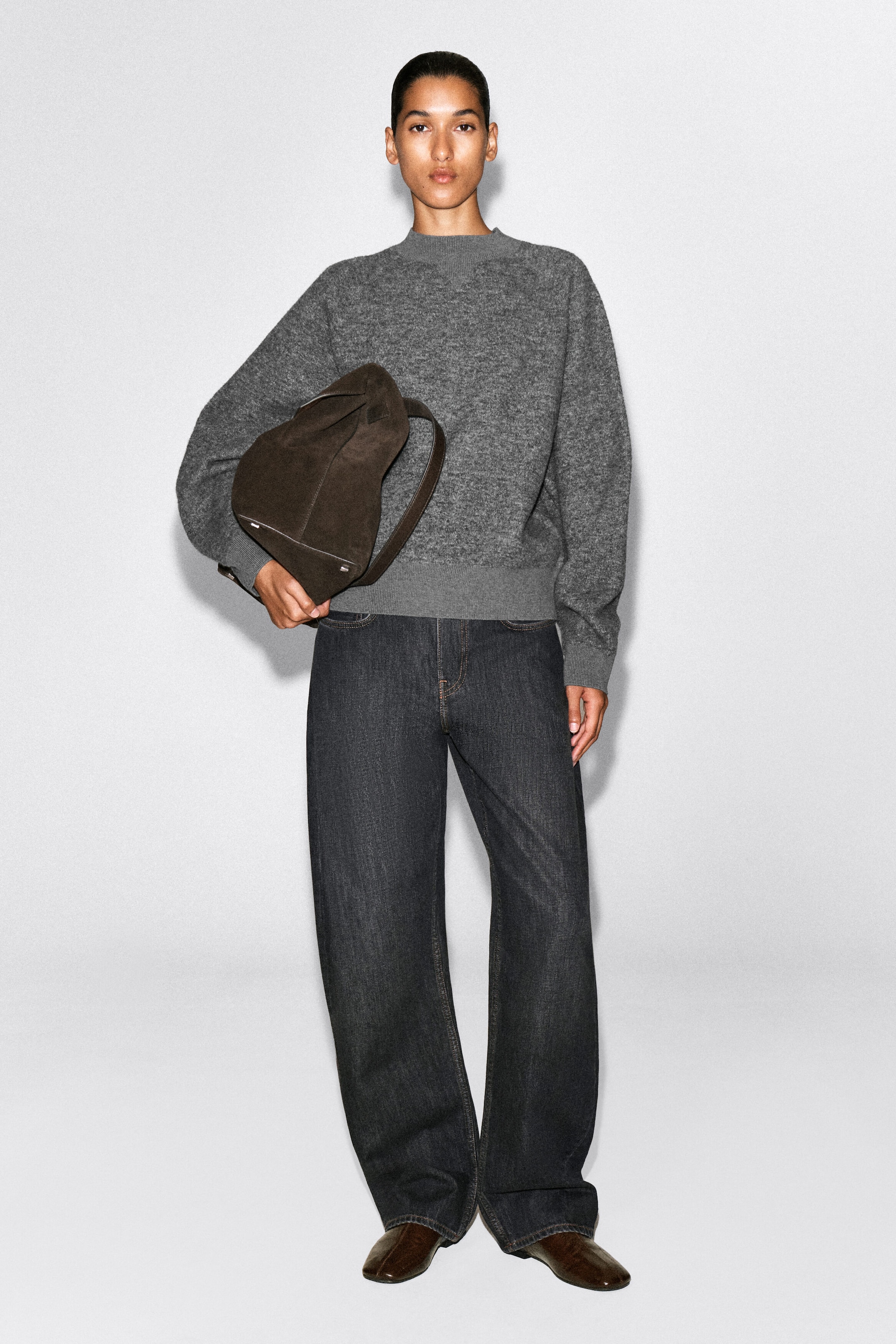 A model is wearing a gray mélange knit crewneck sweater featuring a relaxed fit, ribbed trims, and a V-stitch detail at the neck, paired with dark wash wide-leg jeans. A model is wearing a gray mélange knit crewneck sweater featuring a relaxed fit, ribbed trims, and a V-stitch detail at the neck, paired with dark wash wide-leg jeans.
