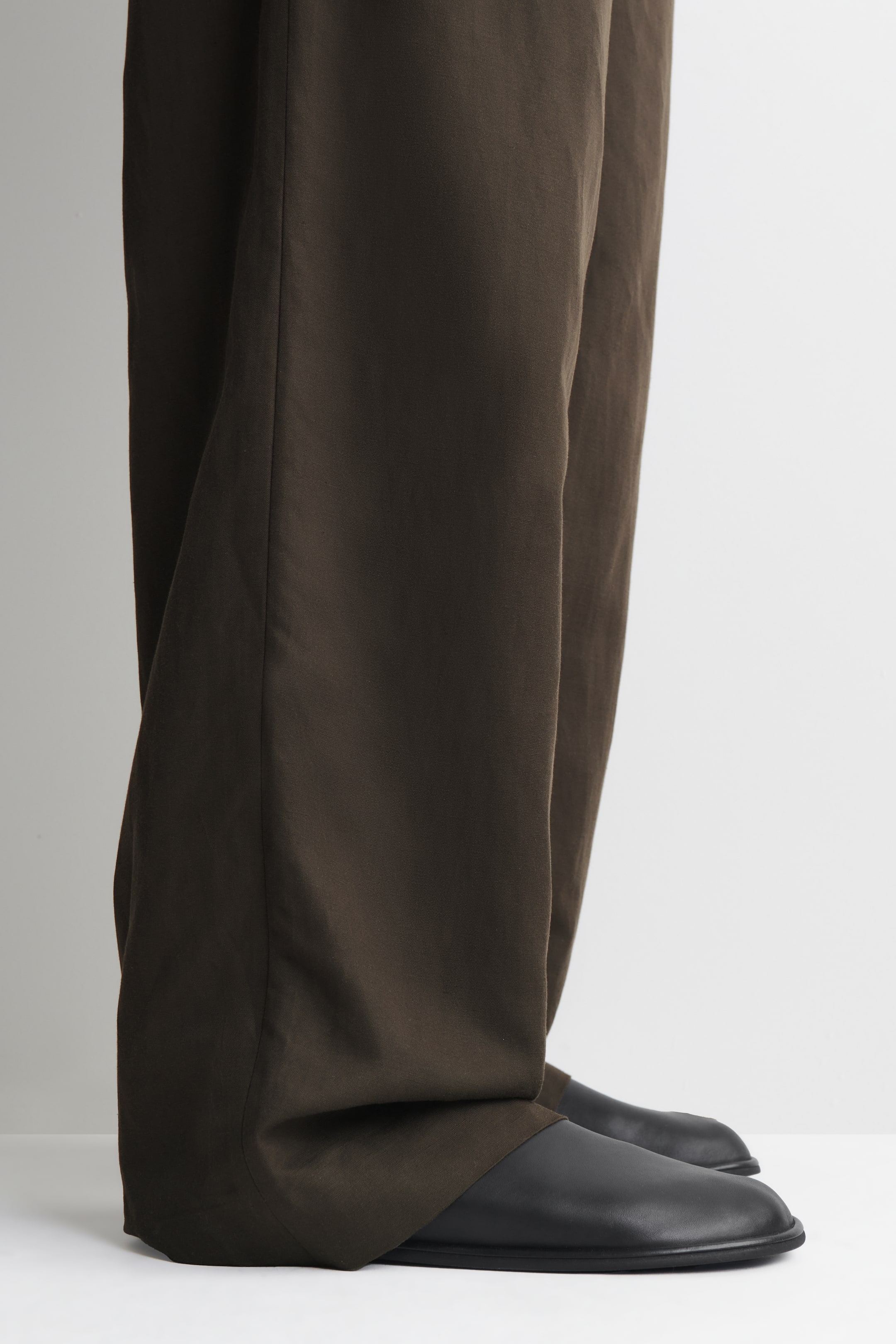 Visualizza l'immagine ingrandita: Pantaloni a gamba larga color marrone scuro che cadono morbidi su scarpe basse nere, visti da un'angolazione laterale-frontale.