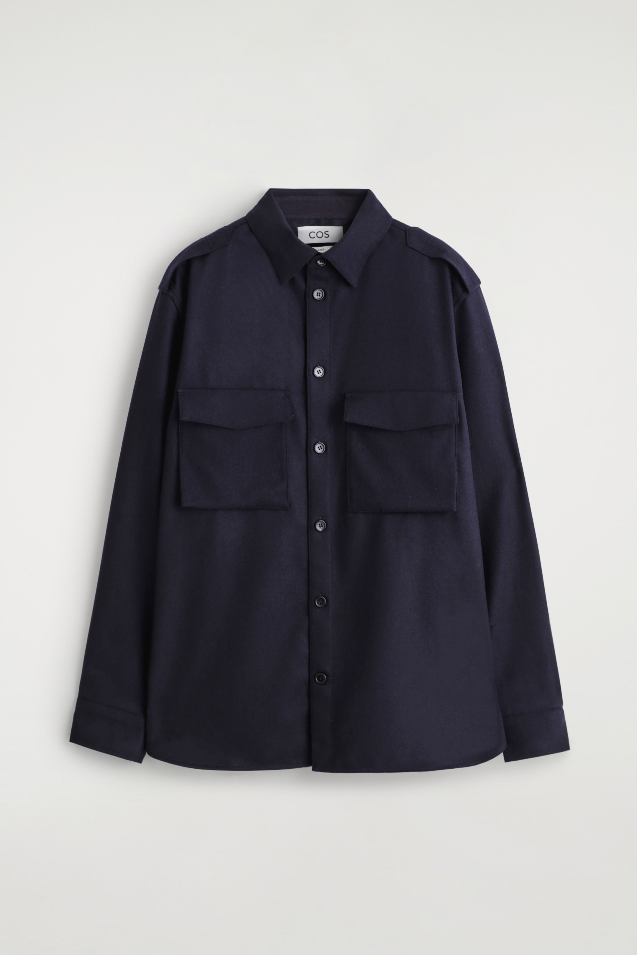 Ingrandisci l'immagine: Una camicia utility blu navy è presentata frontalmente, realizzata in un tessuto misto lana. Presenta un colletto classico, una chiusura con bottoni scuri e due grandi tasche applicate con patte sul petto. I dettagli delle spalline sono visibili sulle spalle, insieme a maniche lunghe che terminano con polsini abbottonati.