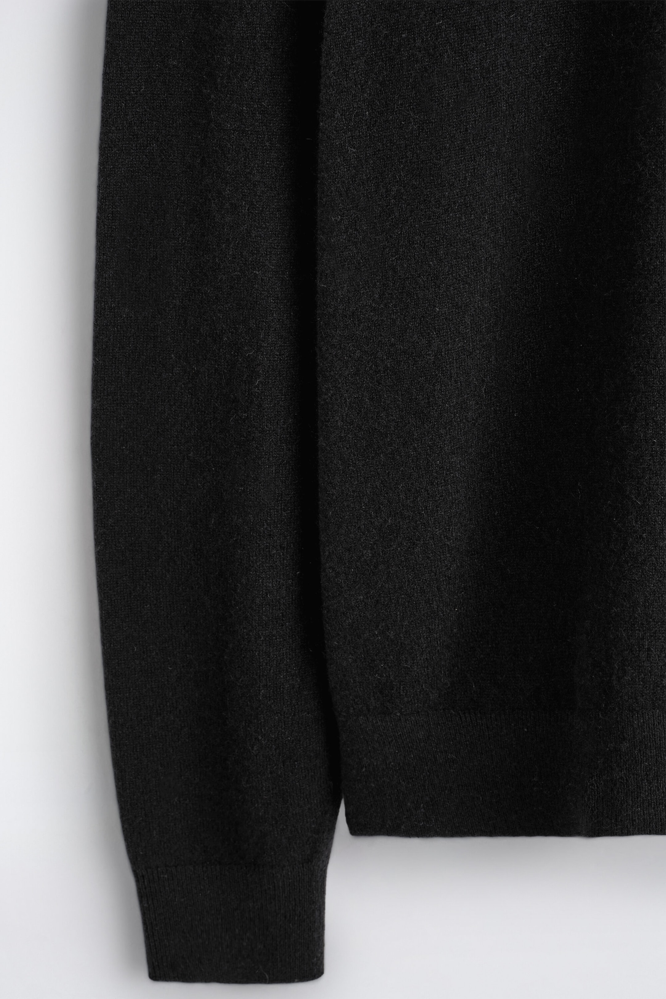This close-up of the black pure cashmere turtleneck sweater showcases its soft, fine-knit texture. The sleeve hangs alongside the body, displaying its ribbed cuff next to the sweater’s ribbed hem. This close-up of the black pure cashmere turtleneck sweater showcases its soft, fine-knit texture. The sleeve hangs alongside the body, displaying its ribbed cuff next to the sweater’s ribbed hem.