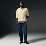 Placeholder for: Person wearing a yellow fuzzy sweater over a plaid shirt, blue jeans, and black loafers, posing against a dark background.