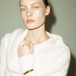Placeholder for: Person with slicked-back hair wearing a cozy white sweater and a gold bracelet, gazing directly at the camera.