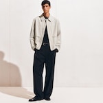 Placeholder for: A person wearing a light beige jacket over a black shirt, with black wide-leg pants and black shoes, standing against a plain background.
