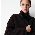 Placeholder for: Person wearing a dark brown wool coat with button details, looking directly at the camera against a plain white background.