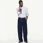 Placeholder for: Model wearing a light blue striped shirt over a black top, with navy blue wide-leg trousers and black shoes, standing with one hand on their neck.