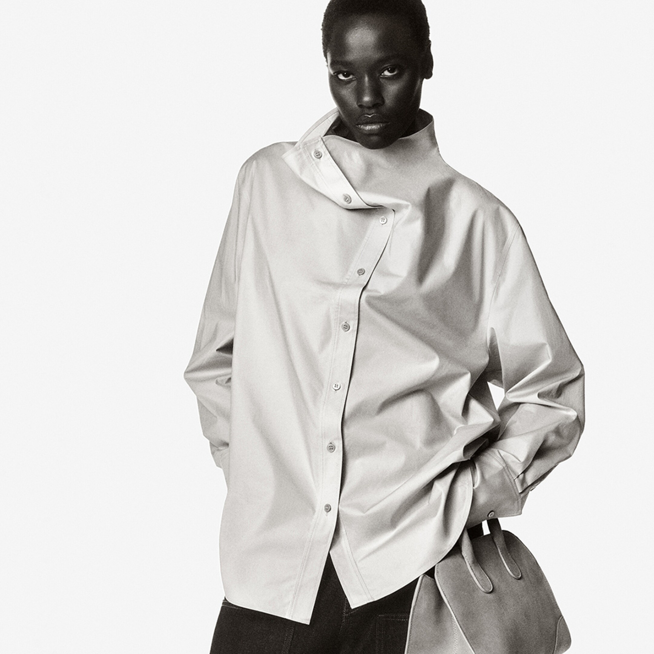 Person in a stylish, oversized button-up shirt with a unique collar design stands confidently, hand in pocket, against a plain background.