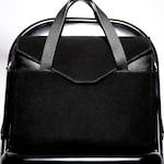Placeholder for: A stylish black leather bag with textured handles rests on a sleek black chair, highlighted against a bright background.