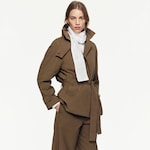 Placeholder for: A woman wearing a brown tailored trench coat with a belted waist and a white scarf, standing against a plain white background.